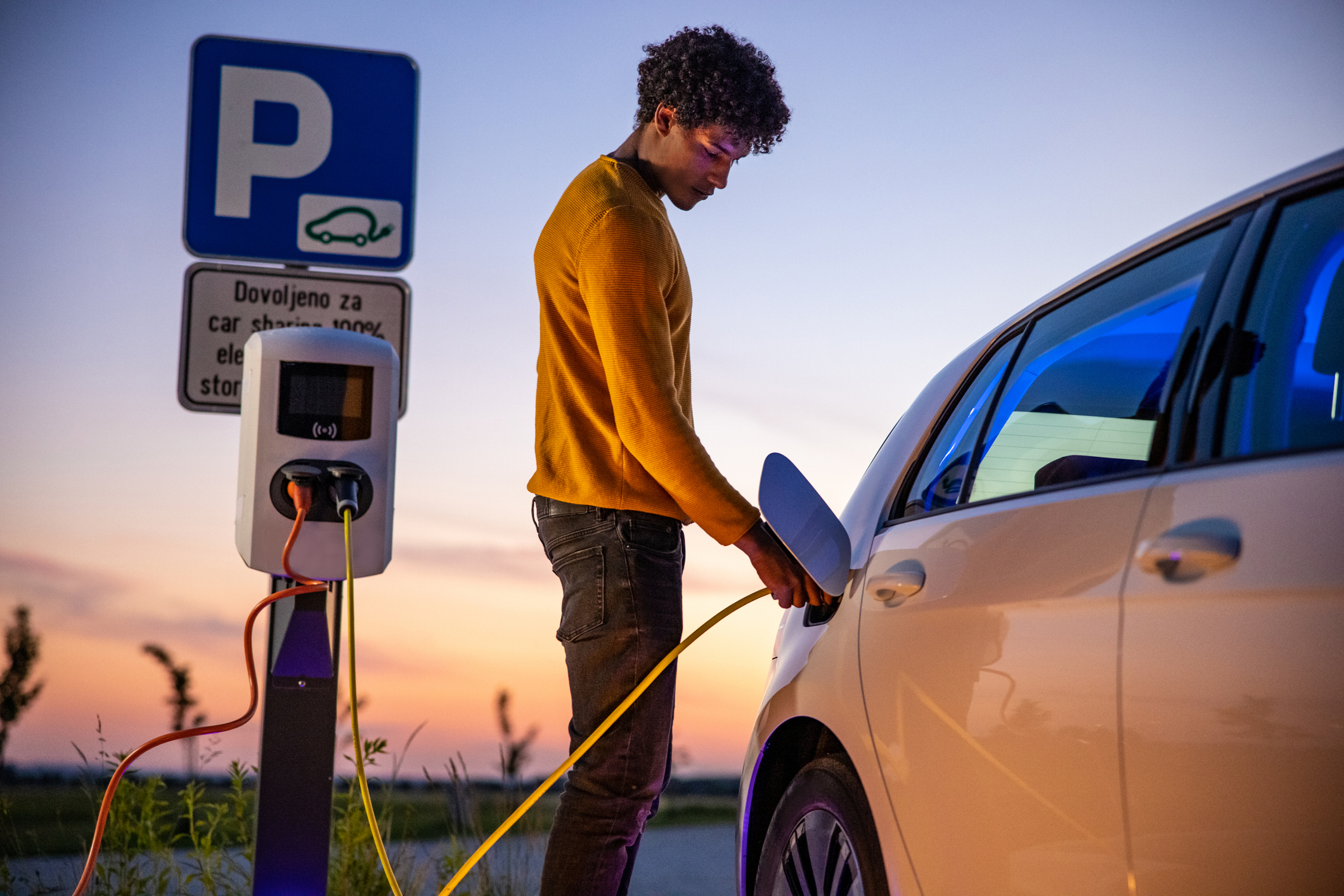 Person charging electric vehicle with nice sunset in background.