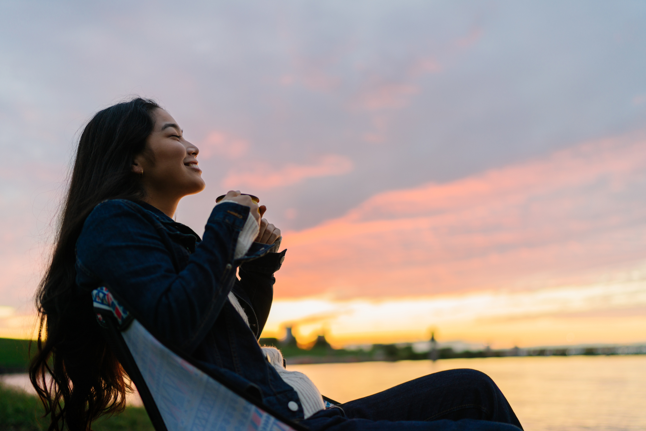 A young person drinks a hot beverage on a lake at sunset