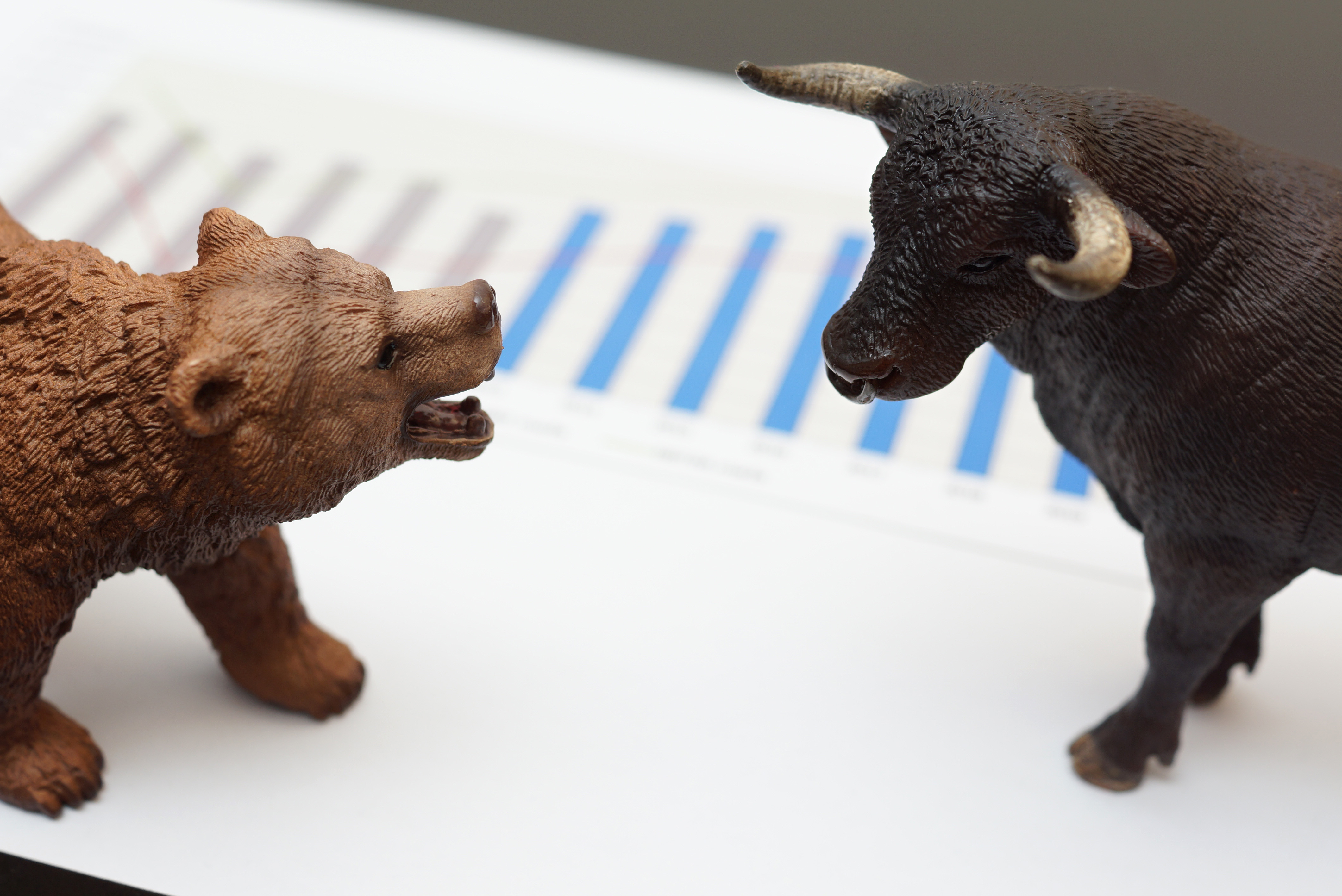 A toy bear and bull standing on a bar graph chart.