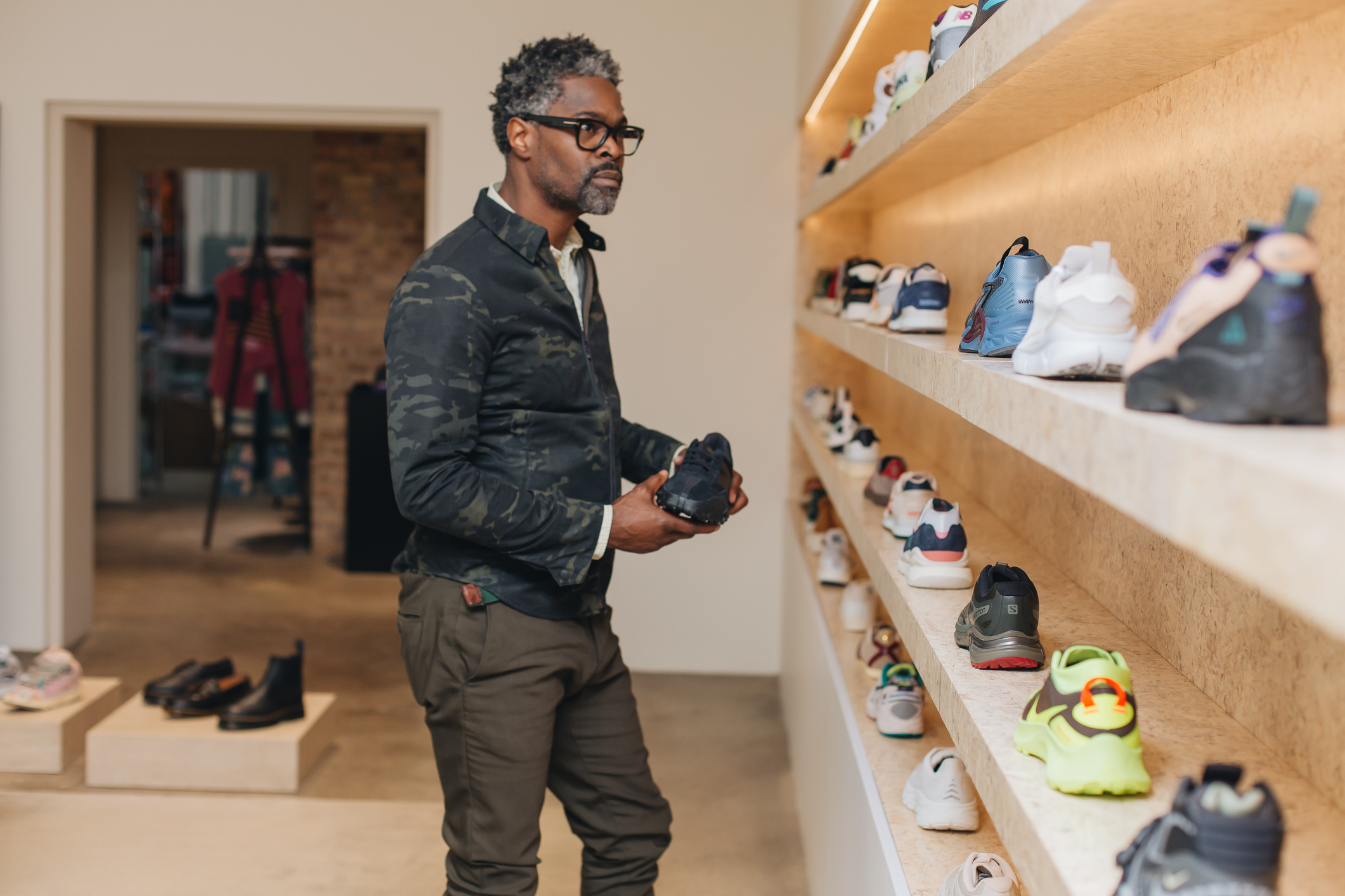 Person holding a shoe and looking at a sneaker display in a shoe store.