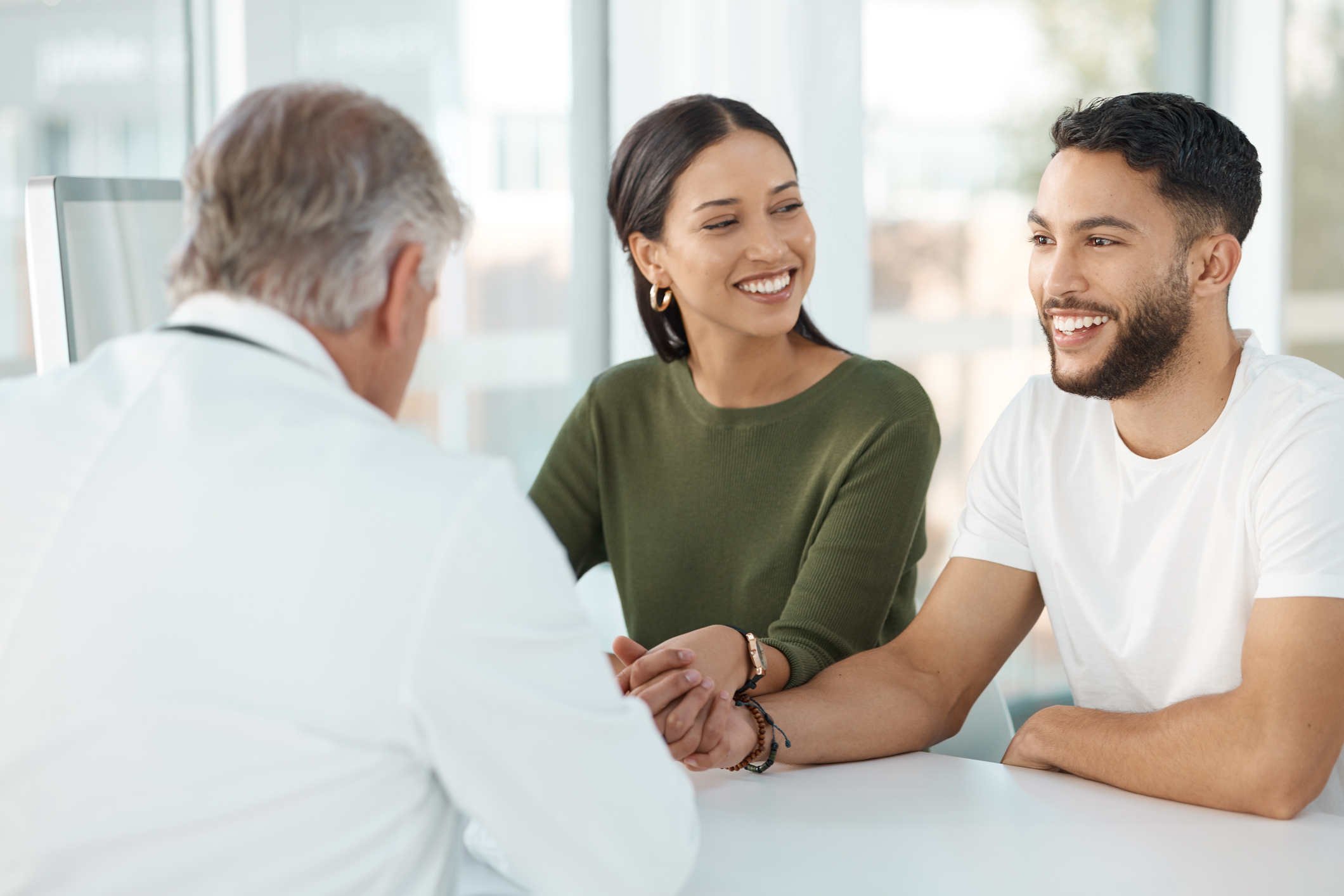a young couple holding hands and smiling while speaking with a doctor