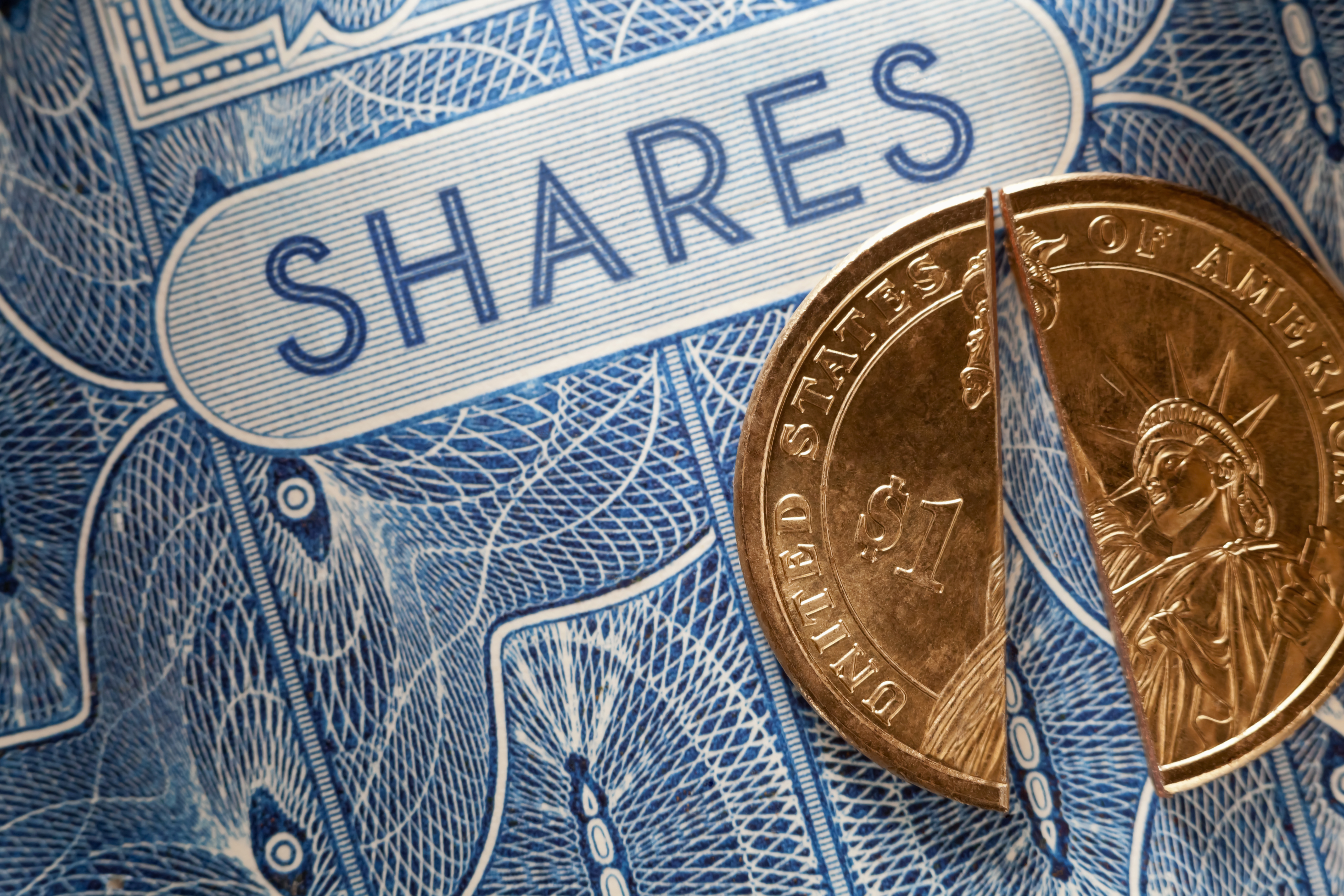 A $1 coin being split in half on top of a blue share certificate.