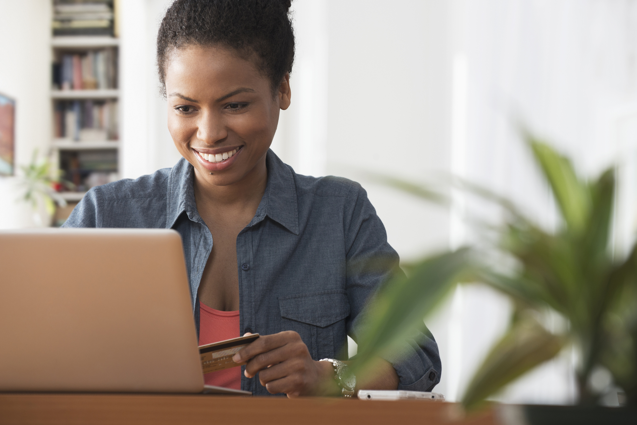 A smiling person contemplating an online purchase while holding a credit card in one hand.