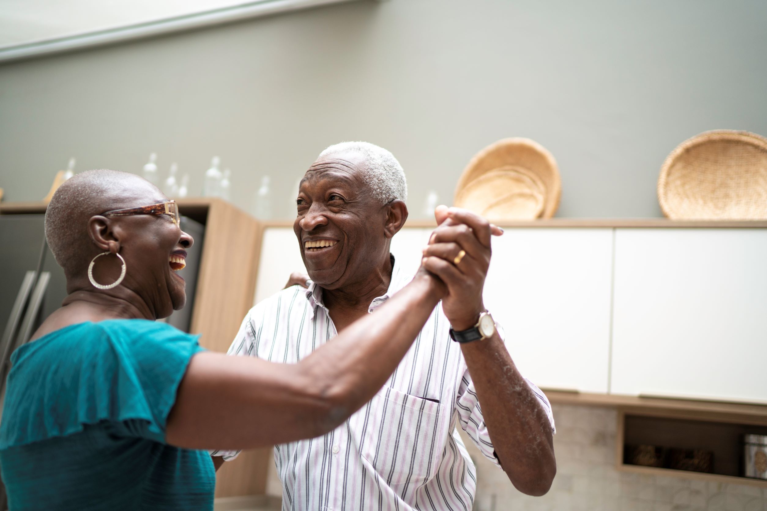Two seniors smiling and dancing in their kitchen.