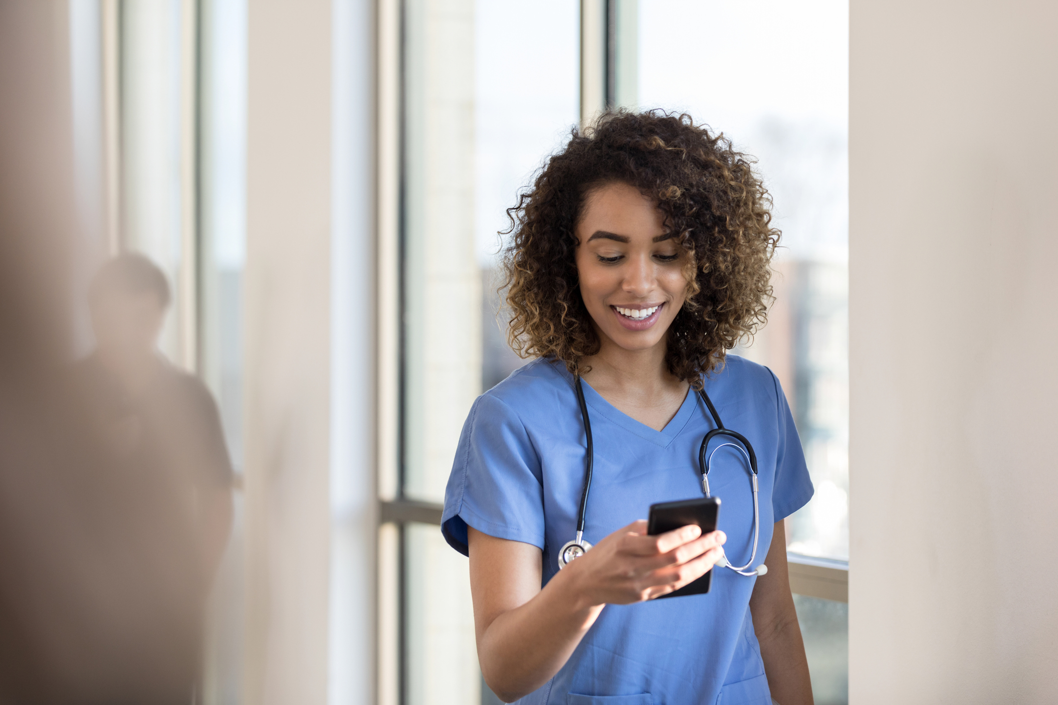 Person in scrubs smiling and looking at a smartphone.