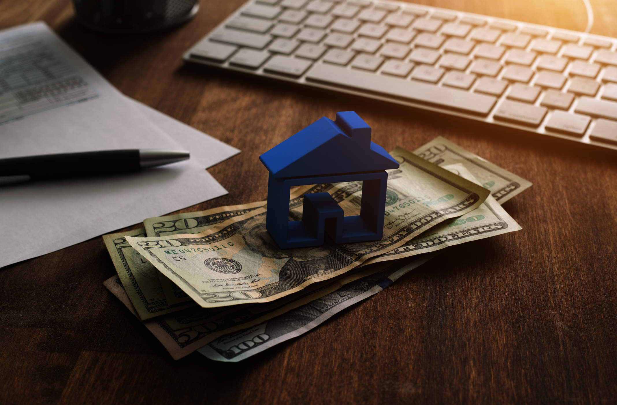 A house paperweight atop a stack of dollar bills on a desk