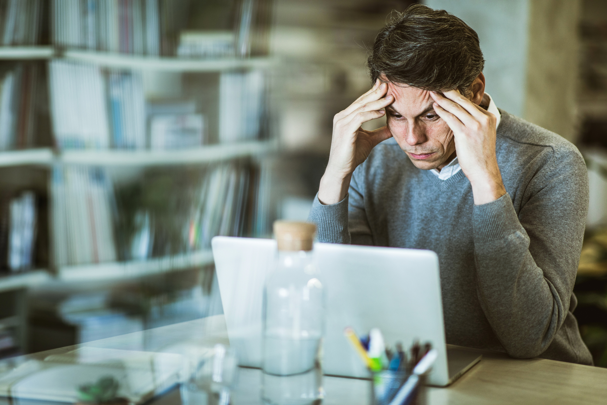 A person rests their forehead in their hands while looking at a laptop.