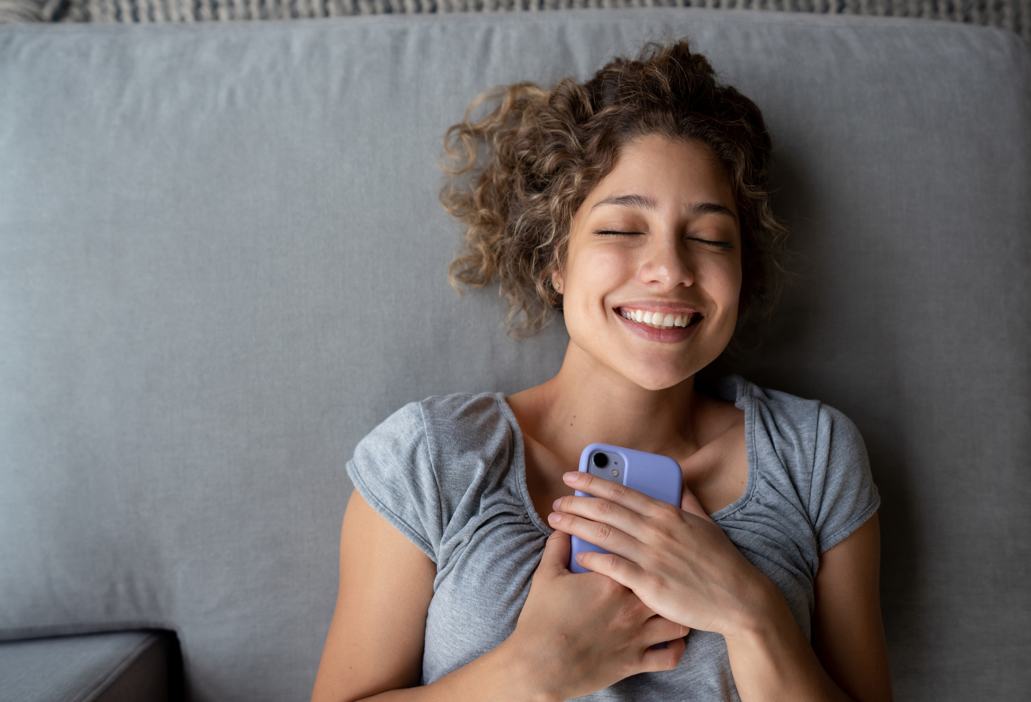 A happy person grasps a smartphone while lying down.