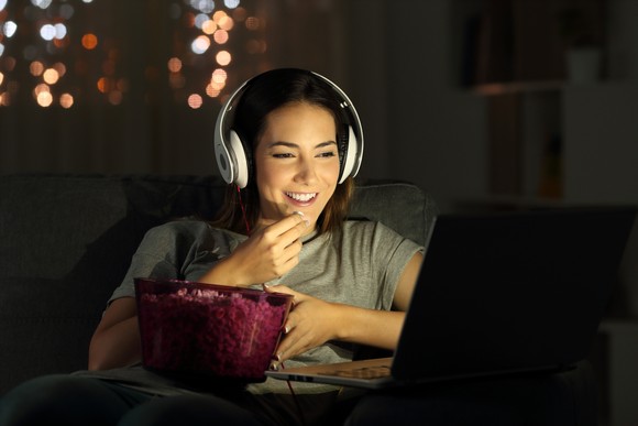 A person watches a streaming video on a laptop while eating popcorn.