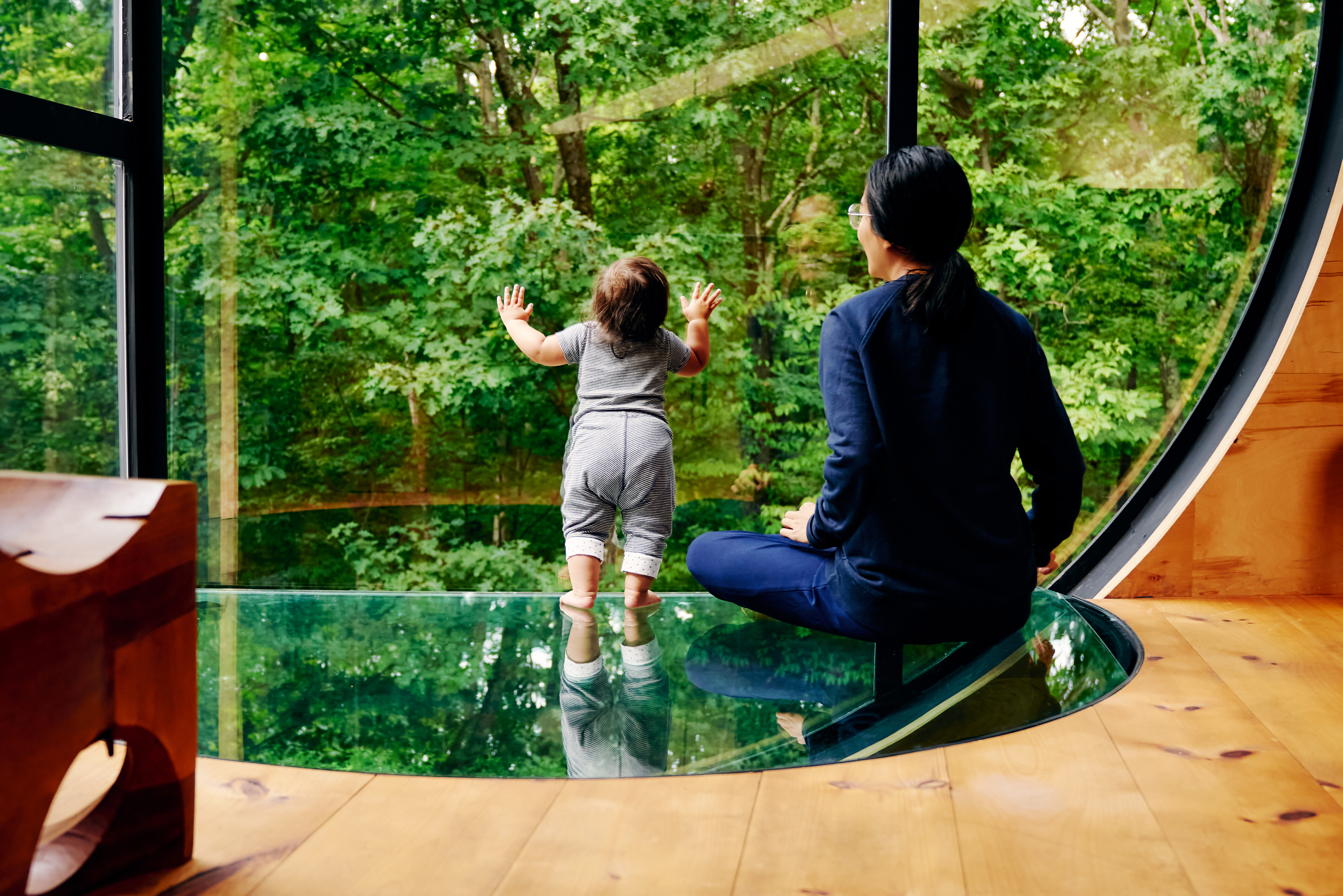 A person and a child looking at trees through a glass window
