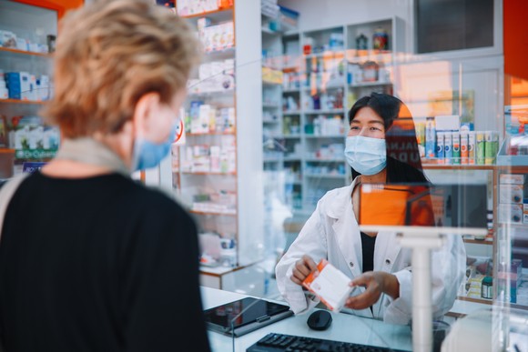 A person picks up a prescription at a pharmacy.