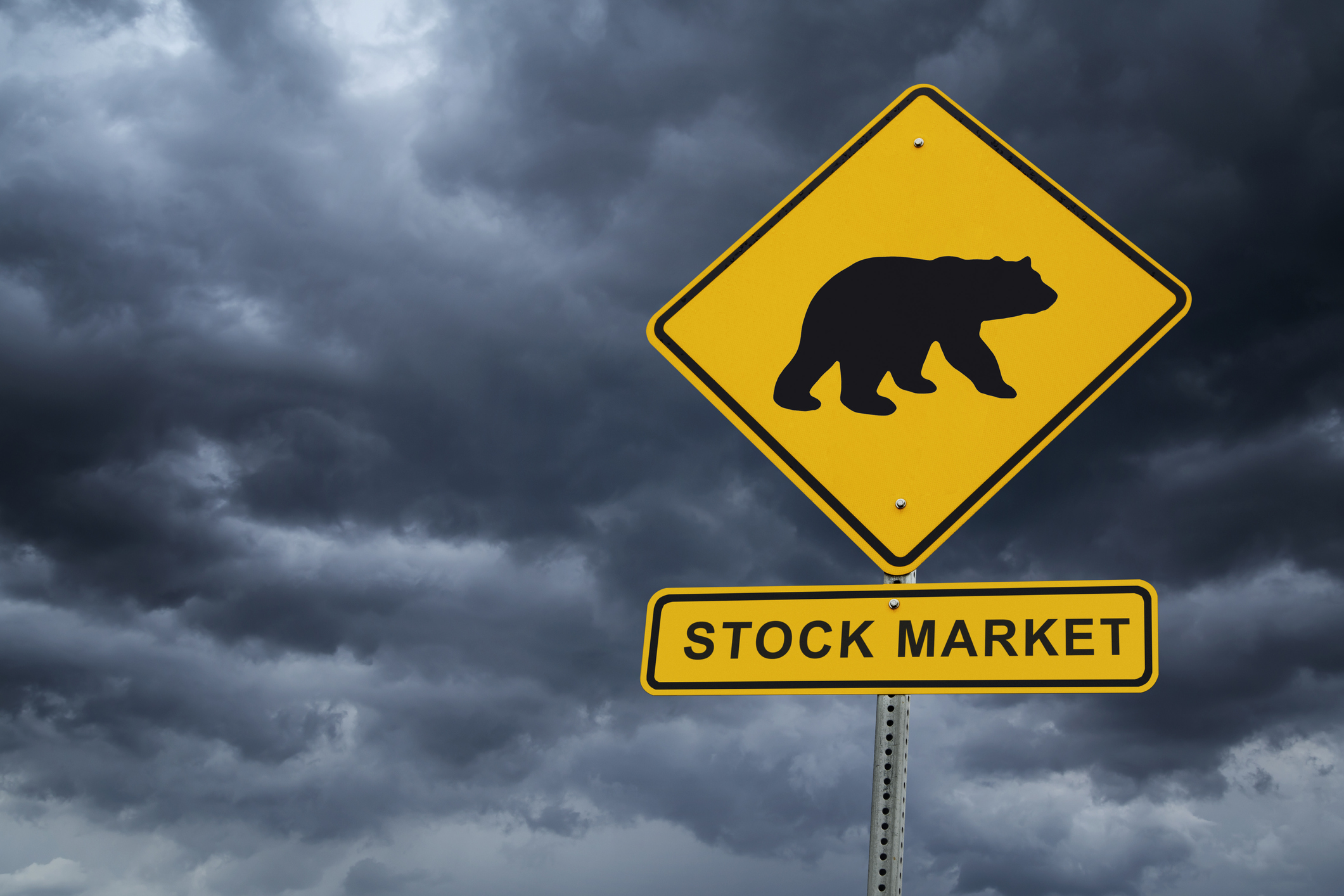 A bear silhouette on a road sign with "stock market" underneath and dark clouds in the background.