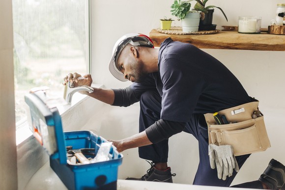 A plumber repairs a bathtub faucet in a home. 