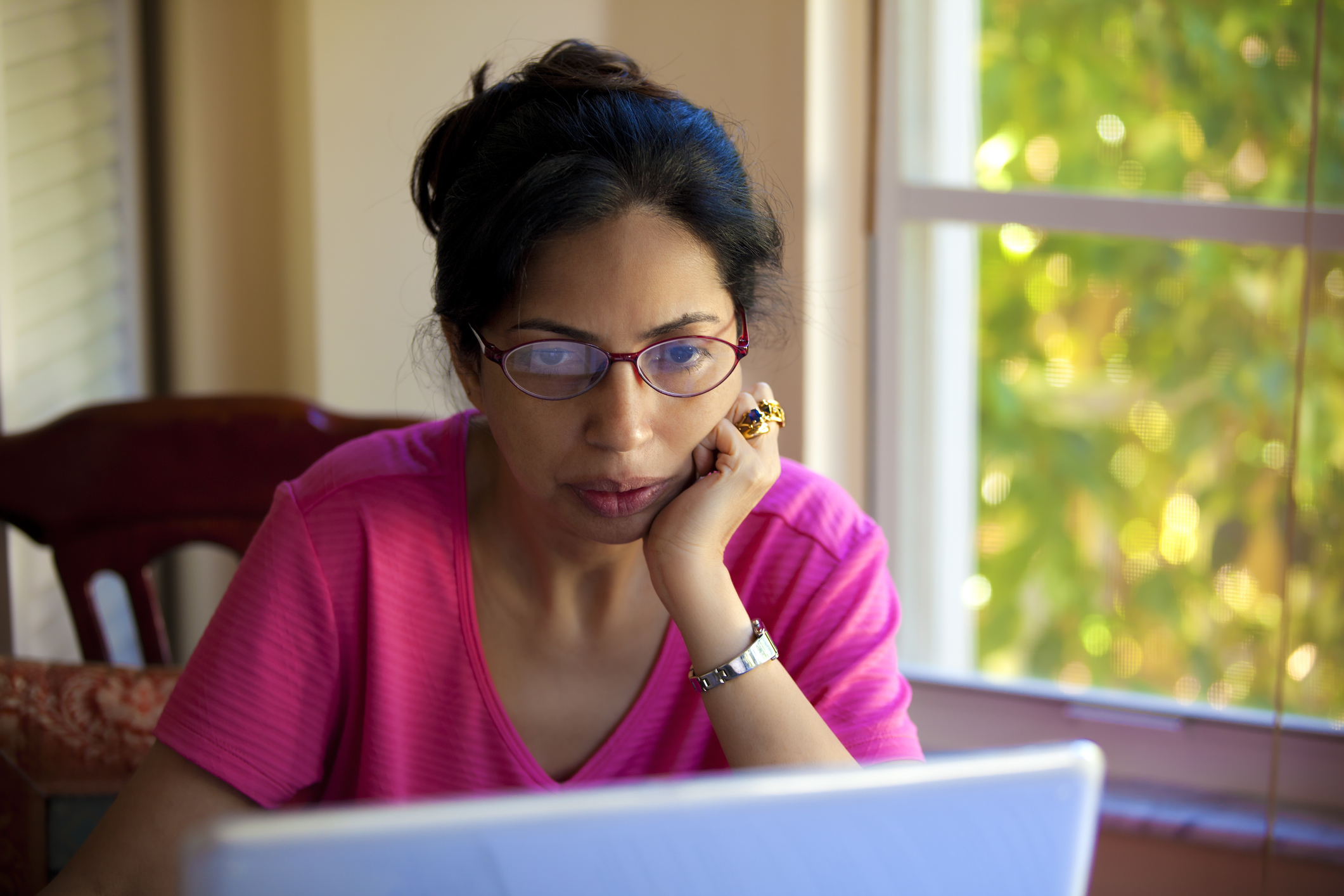 Serious person with hand on chin looking at laptop.