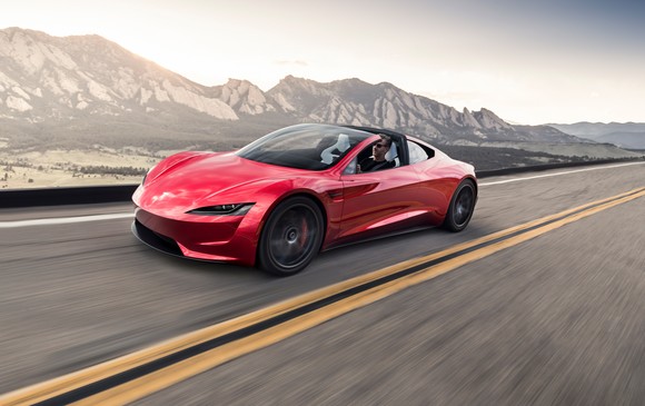 A Red 2022 Tesla Roadster drives down a road with mountains in the background