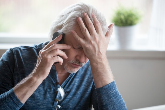A person rests their forehead in their hand while holding a smartphone up to their ear.