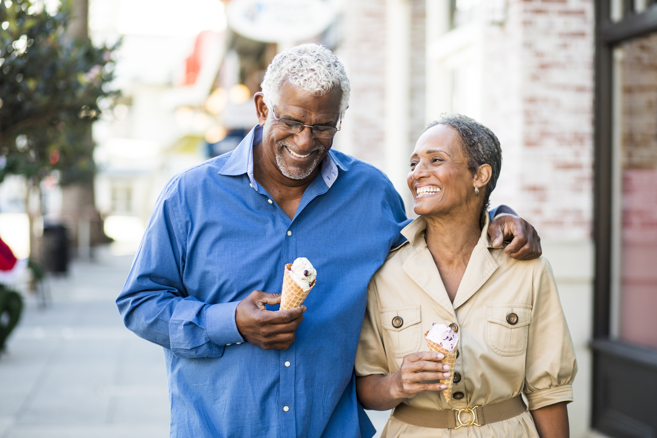 A couple is walking outdoors, smiling, with ice cream cones.
