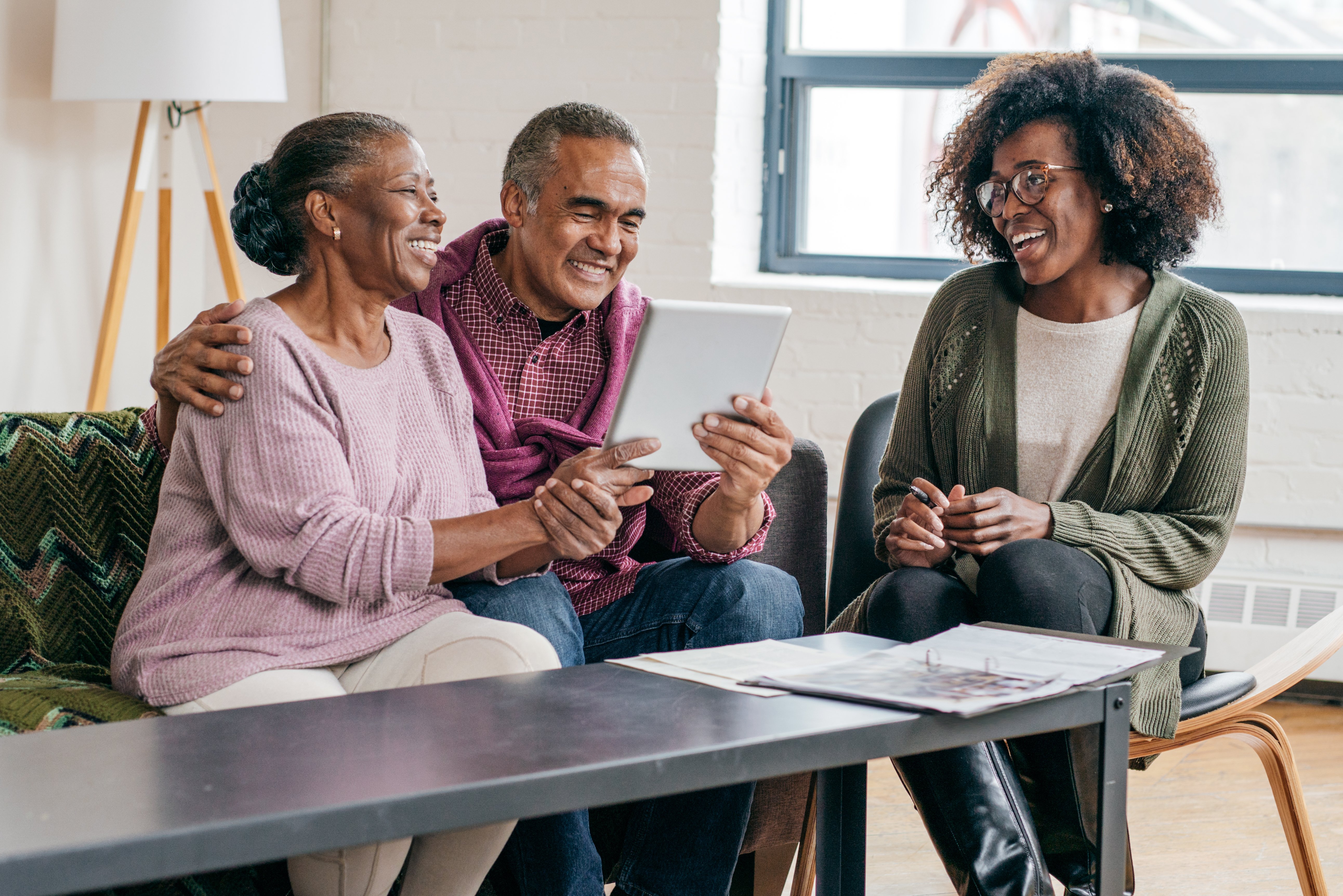 Three people sitting at a table looking at a tablet and smiling.
