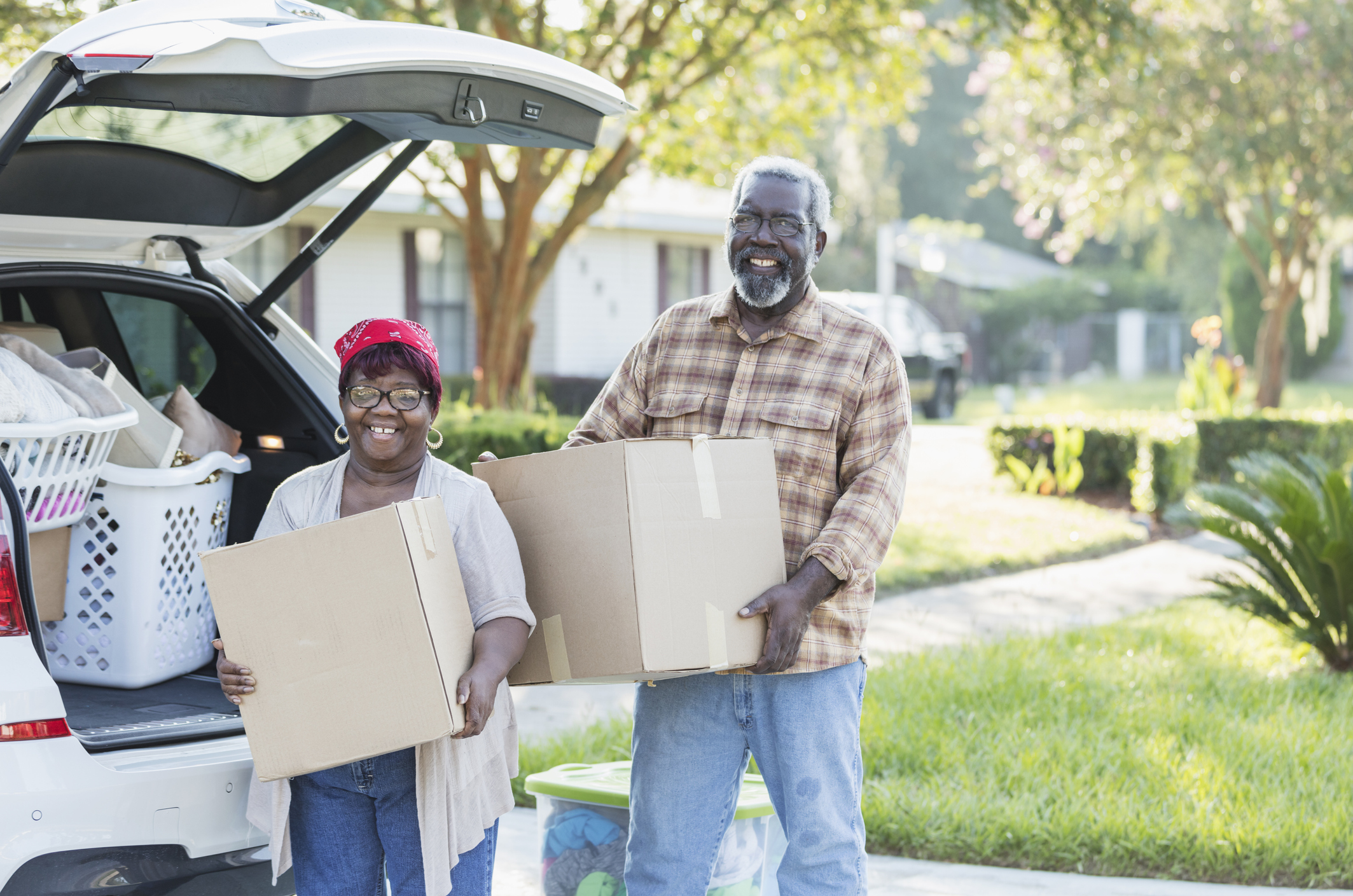 Two smiling people holding moving boxes next to a car.