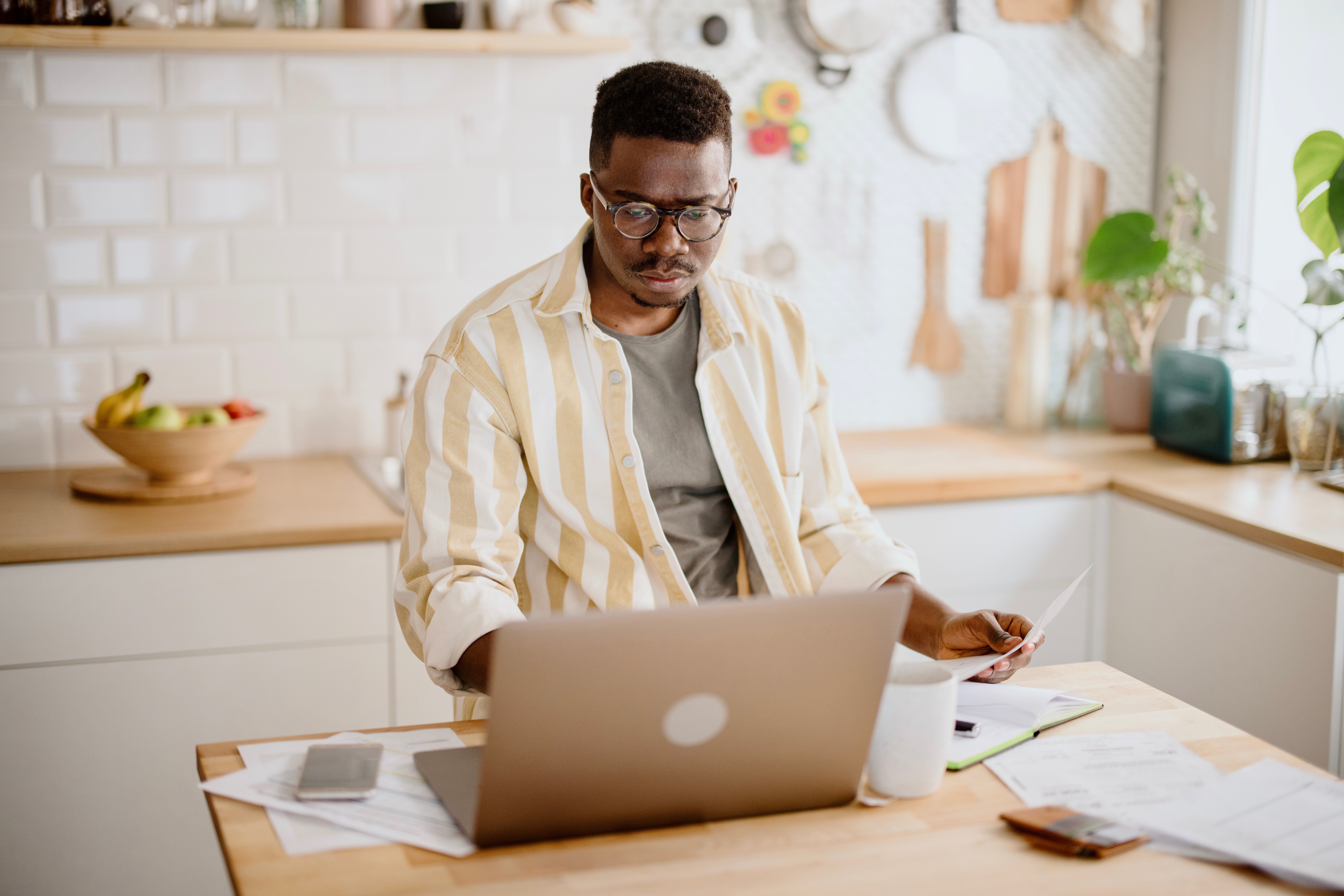 Person looking at an open laptop on a kitchen island while holding a piece of paper.