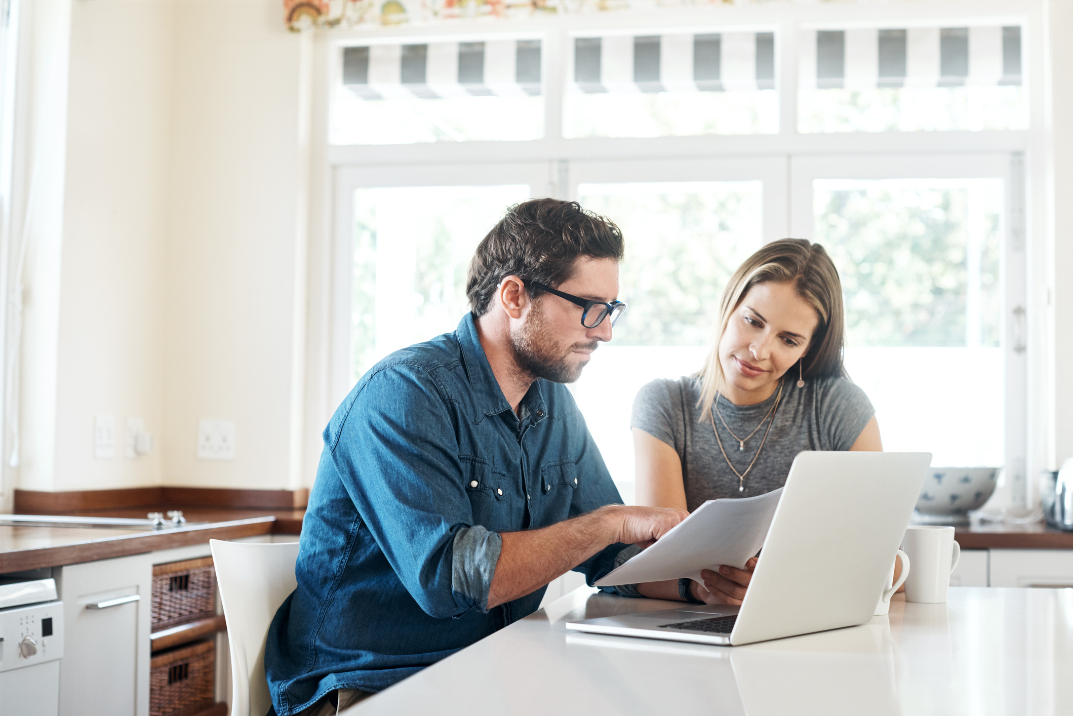 Couple looking at documents and a laptop in their kitchen.