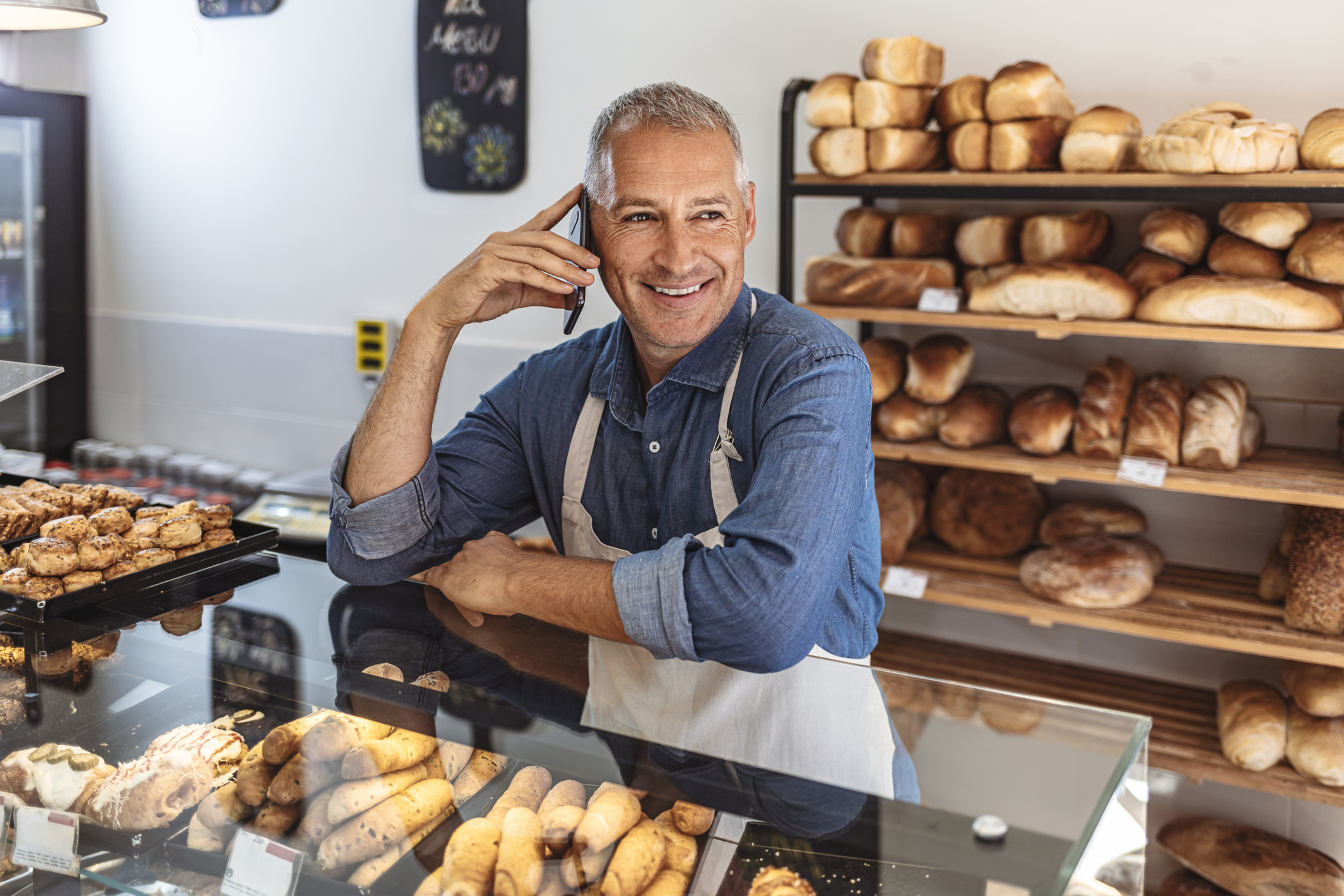 A smiling person in an apron behind a bakery counter.