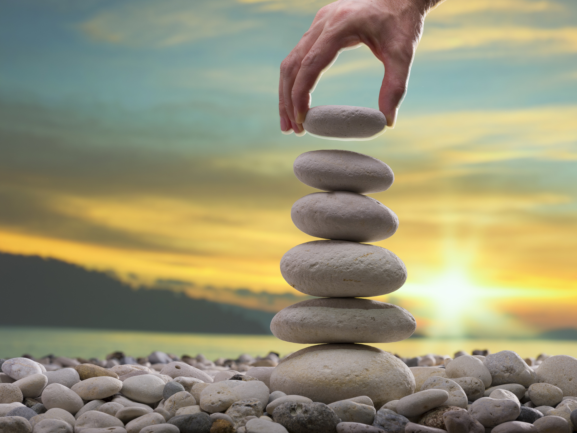 Stacking stones on top of a tower of stones in front of a sunset.