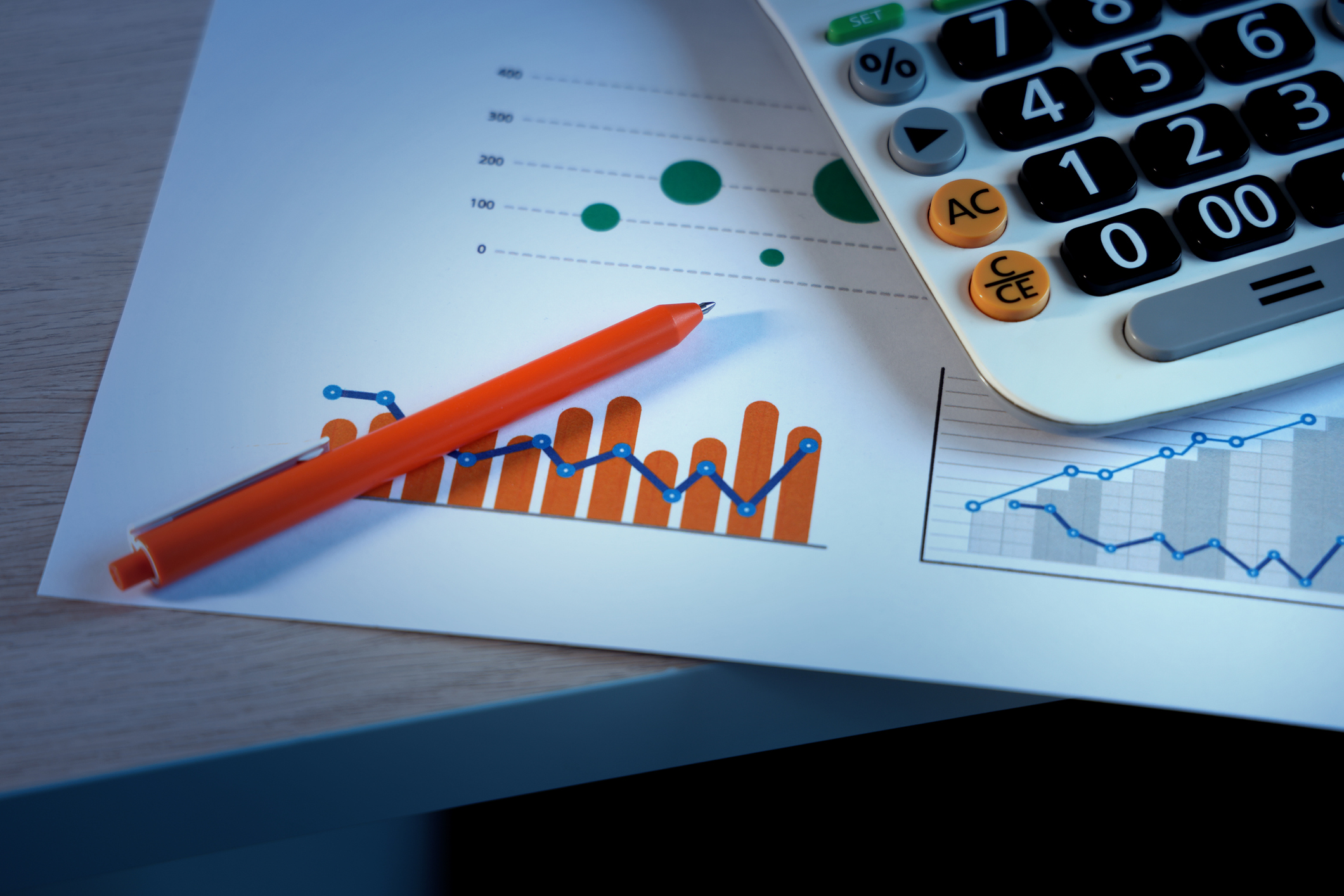 A red pen and a calculator sit atop a document showing financial charts.