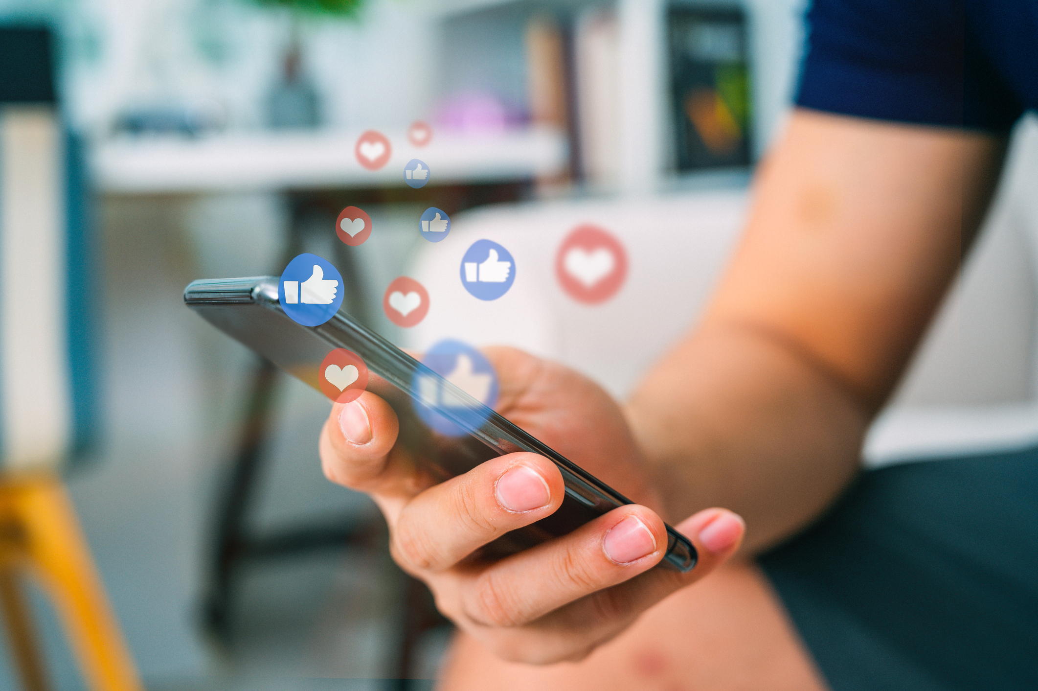 Hand scrolling through smartphone with social media likes and hearts floating over it.