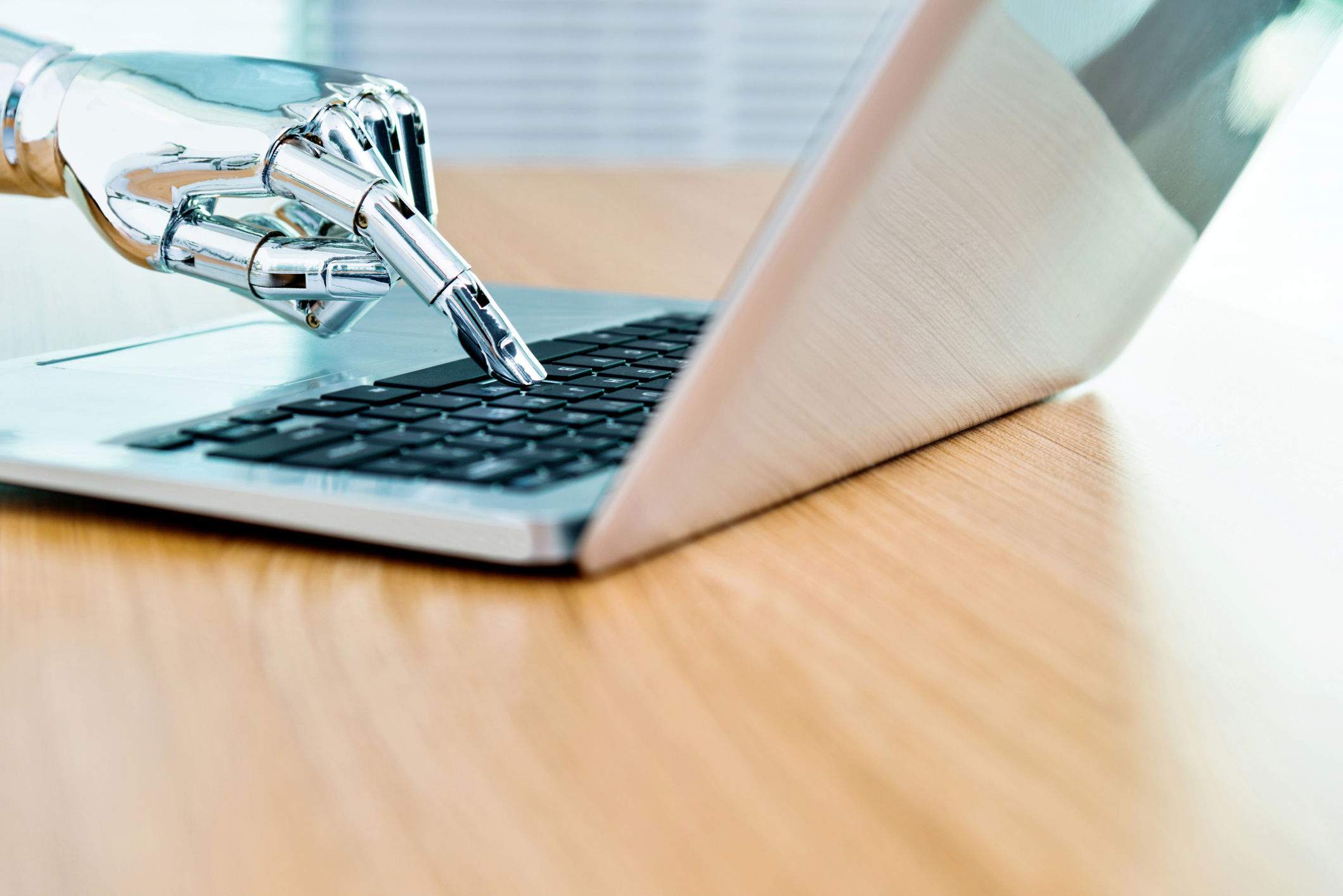 Shiny, metallic rbotic hand typing on a laptop computer.
