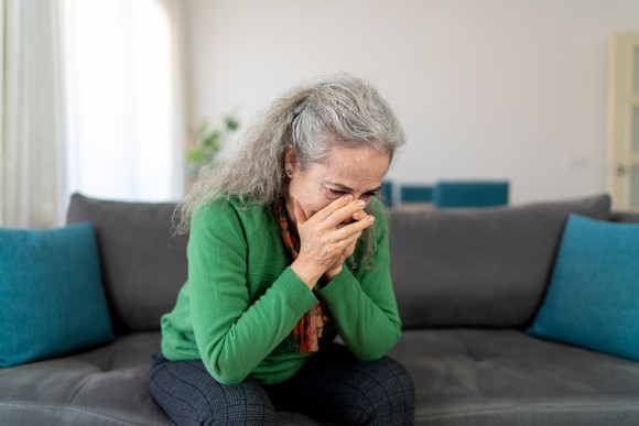 A person sitting on a couch with their hands over part of their face.