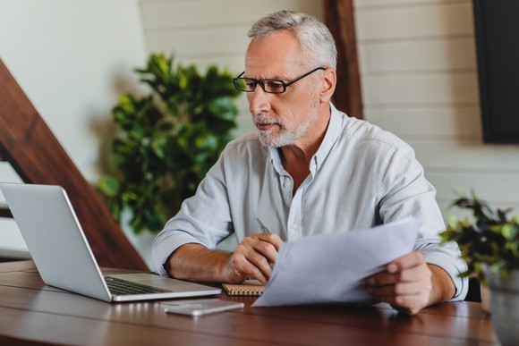A person at a laptop holding papers.