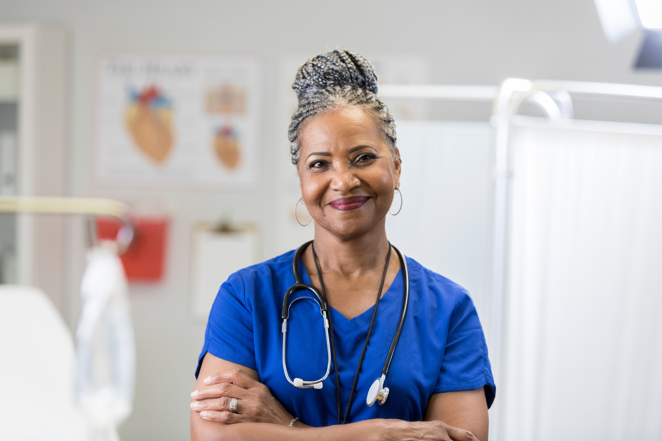 A health care worker is facing the camera, arms crossed, and smiling.