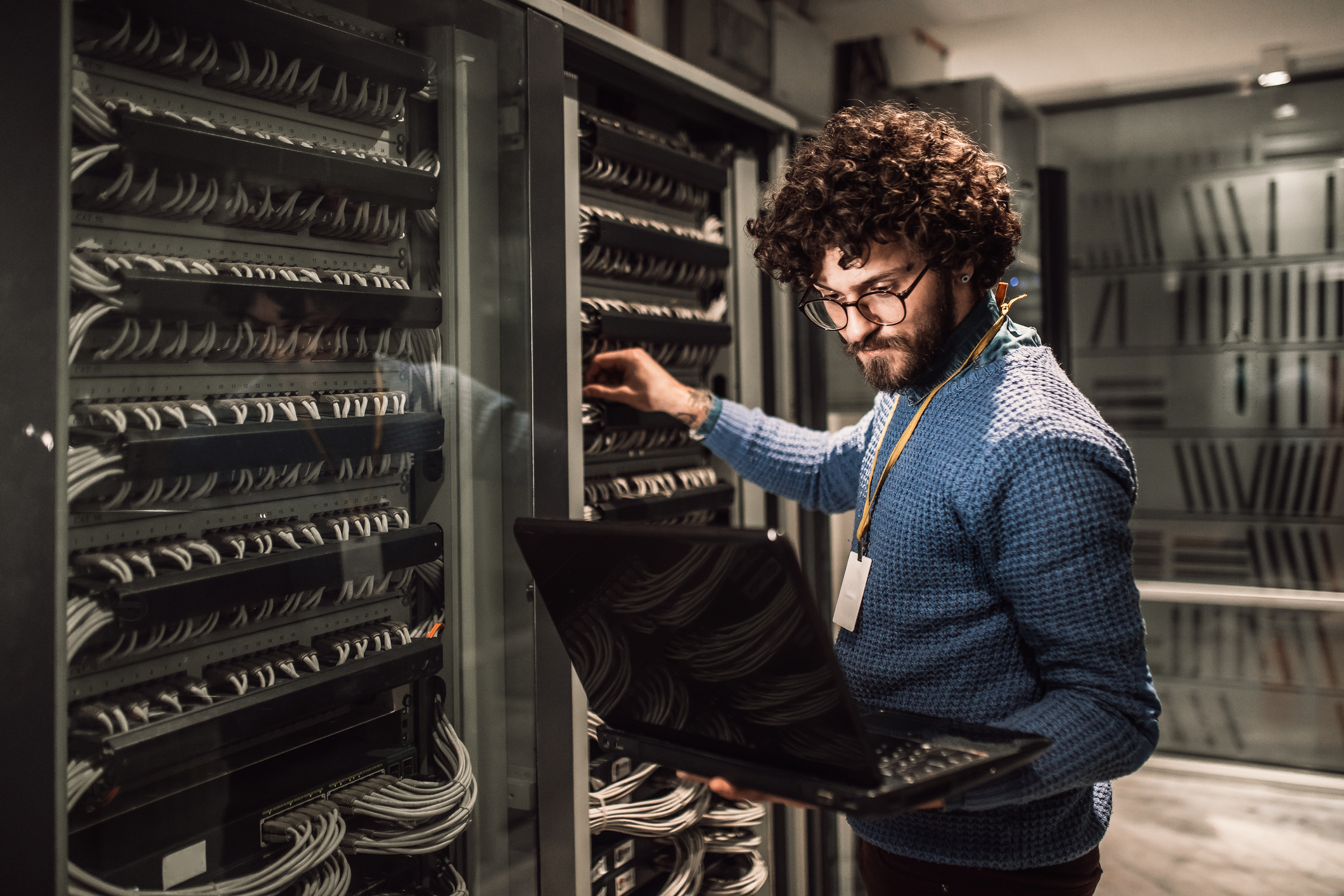 A person performing maintenance in a server room while looking at a laptop.