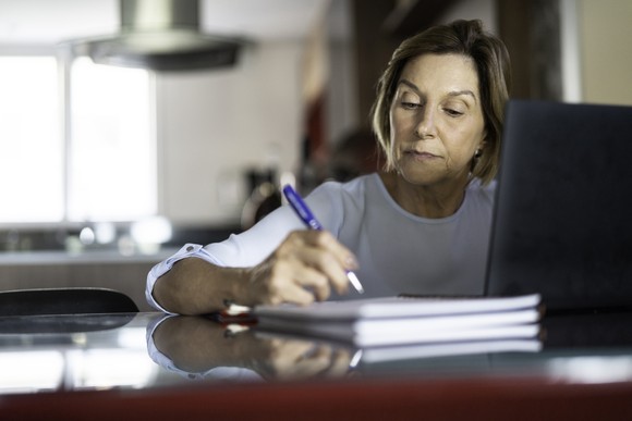 A person at a laptop holding a pen.