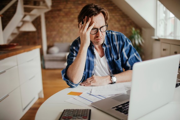 A person at a laptop holding their head.
