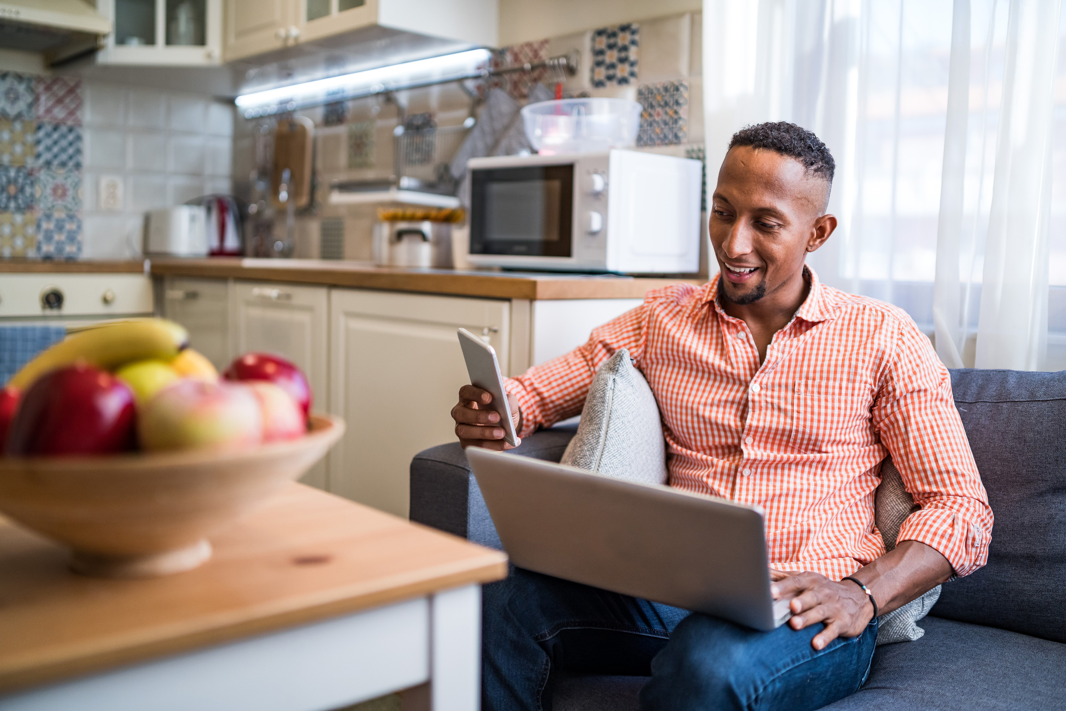 A seated person with an open laptop on their lap who's looking at a smartphone in their right hand.
