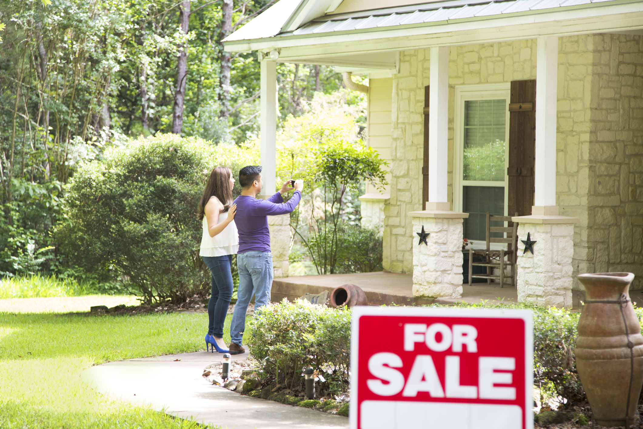 Two people photographing house with a For Sale sign.