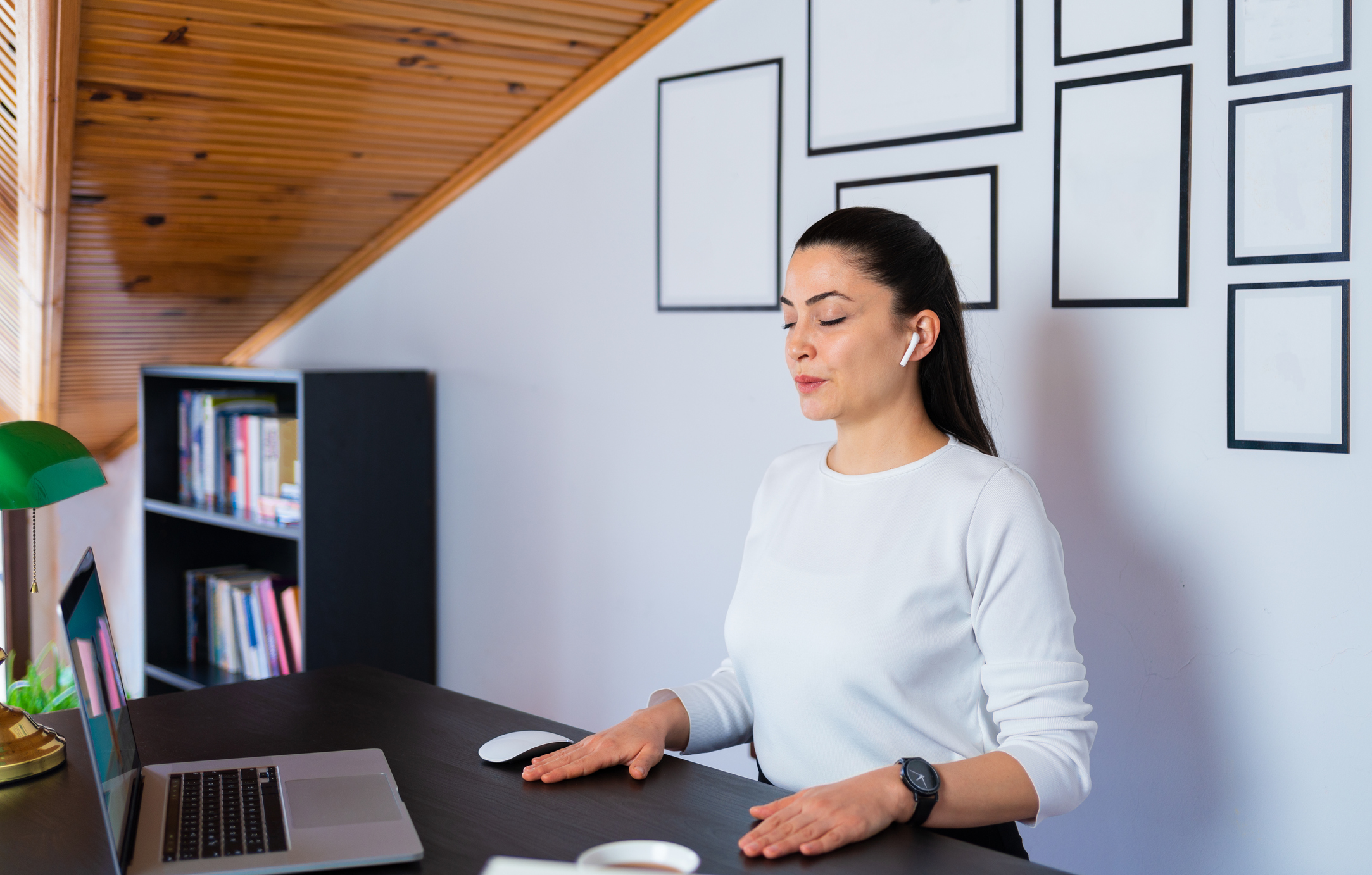 A person closing their eyes and resting their hands on a desk.