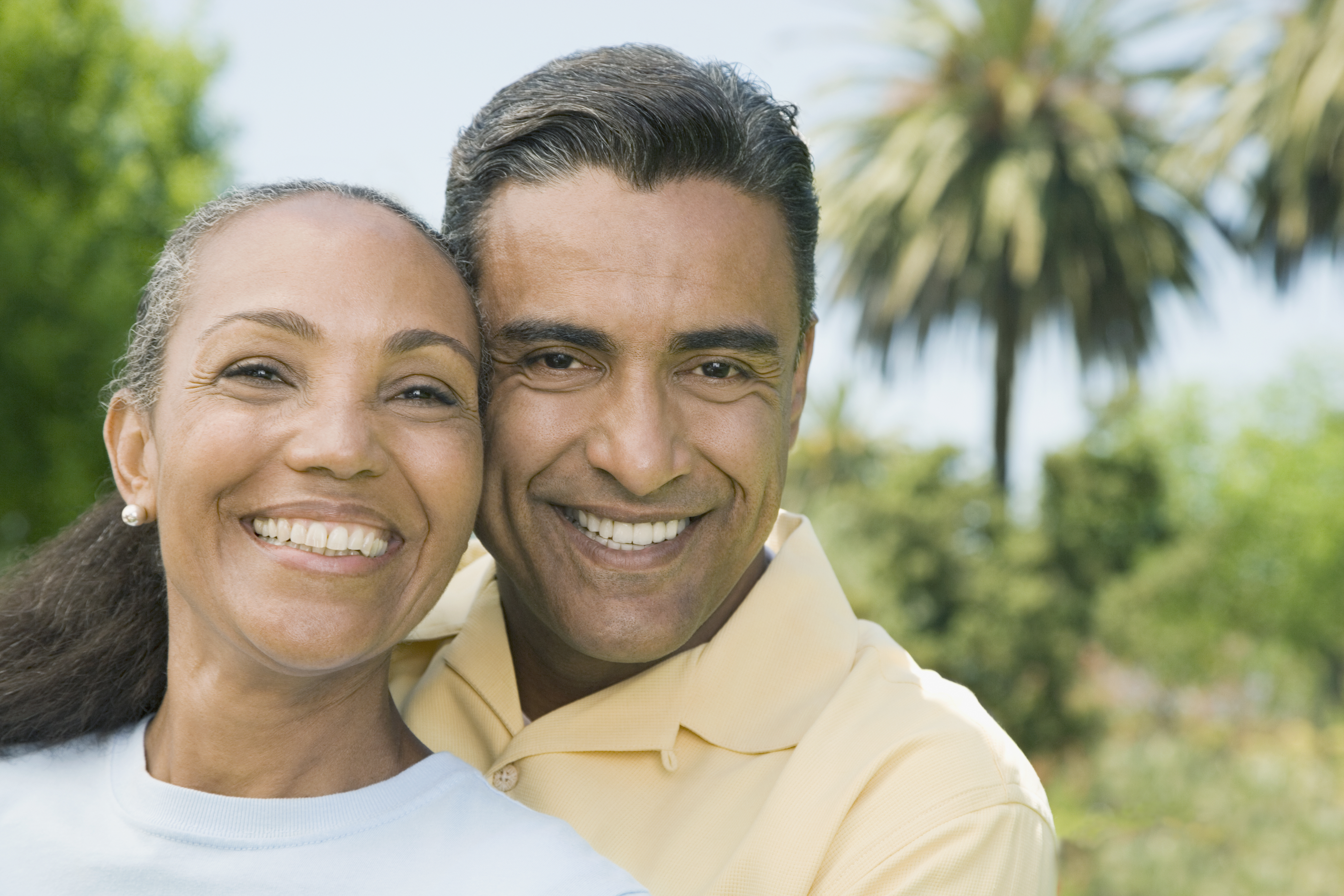 Two people hugging and posing for the camera with trees behind them.