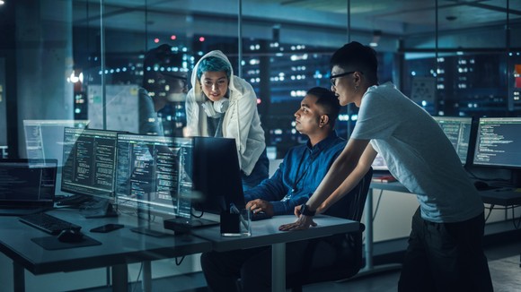 Three cybersecurity professionals work together at a workstation.