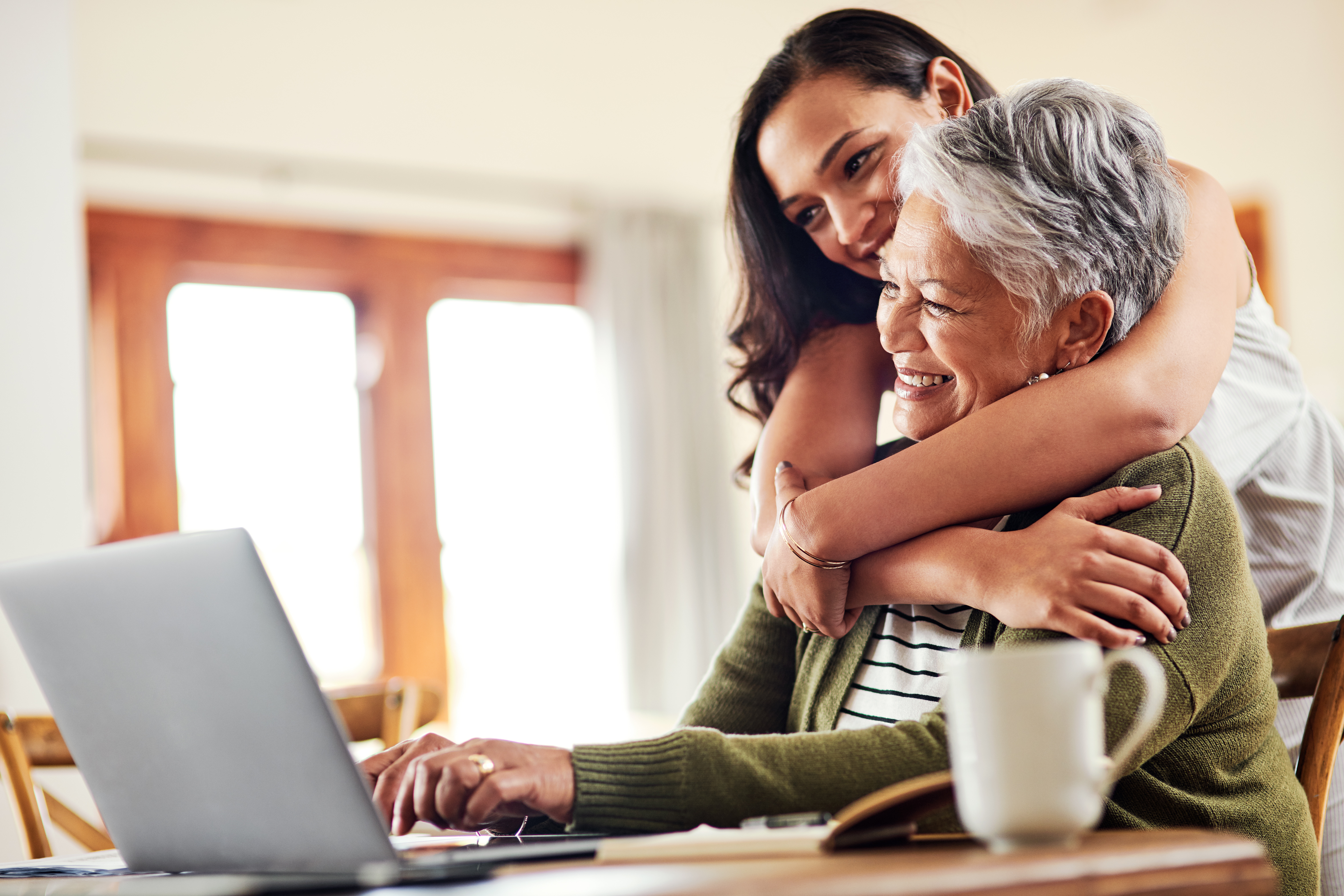 Two people happily looking at laptop, one hugging the other.