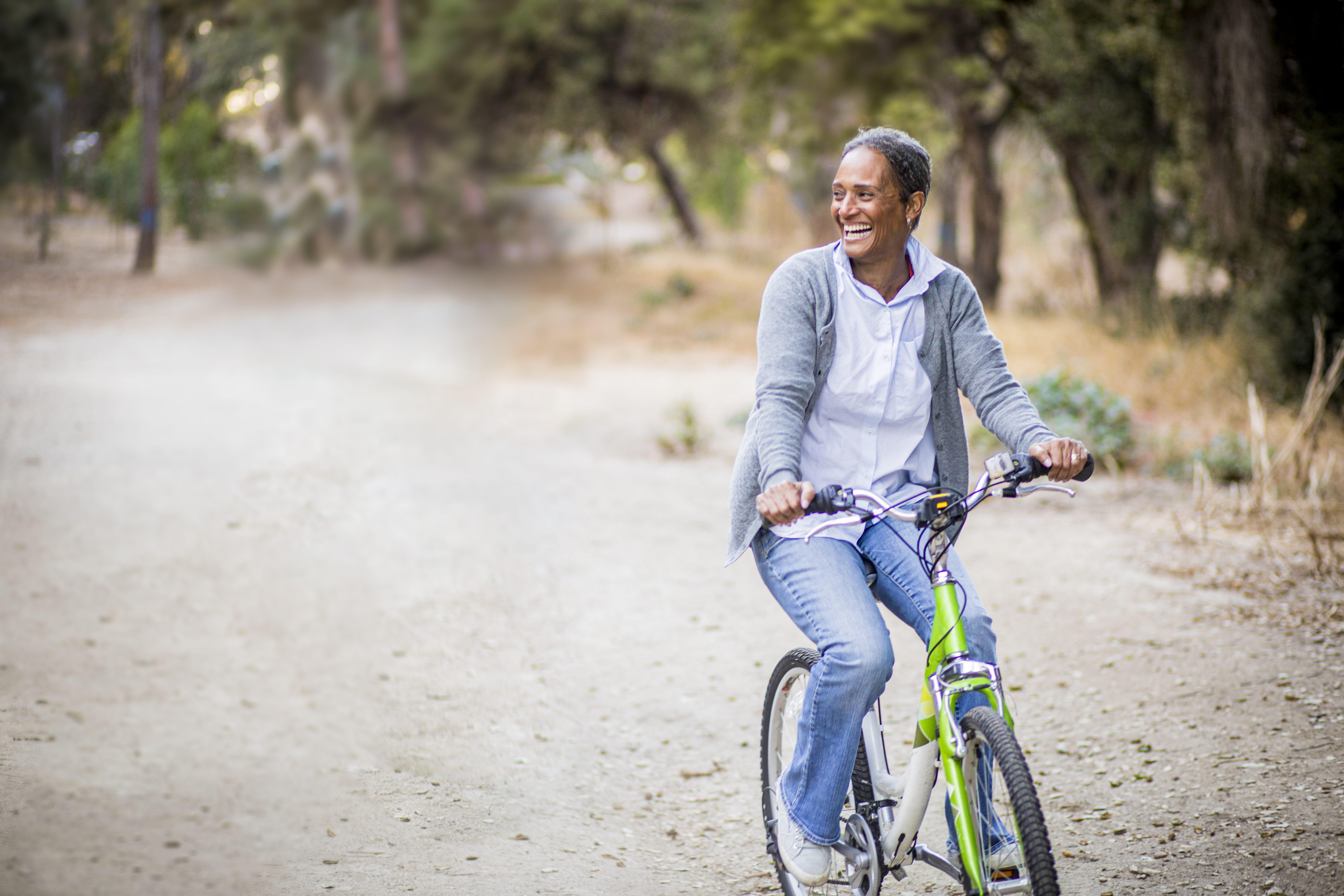 A person smiles while riding their bicycle through the park.