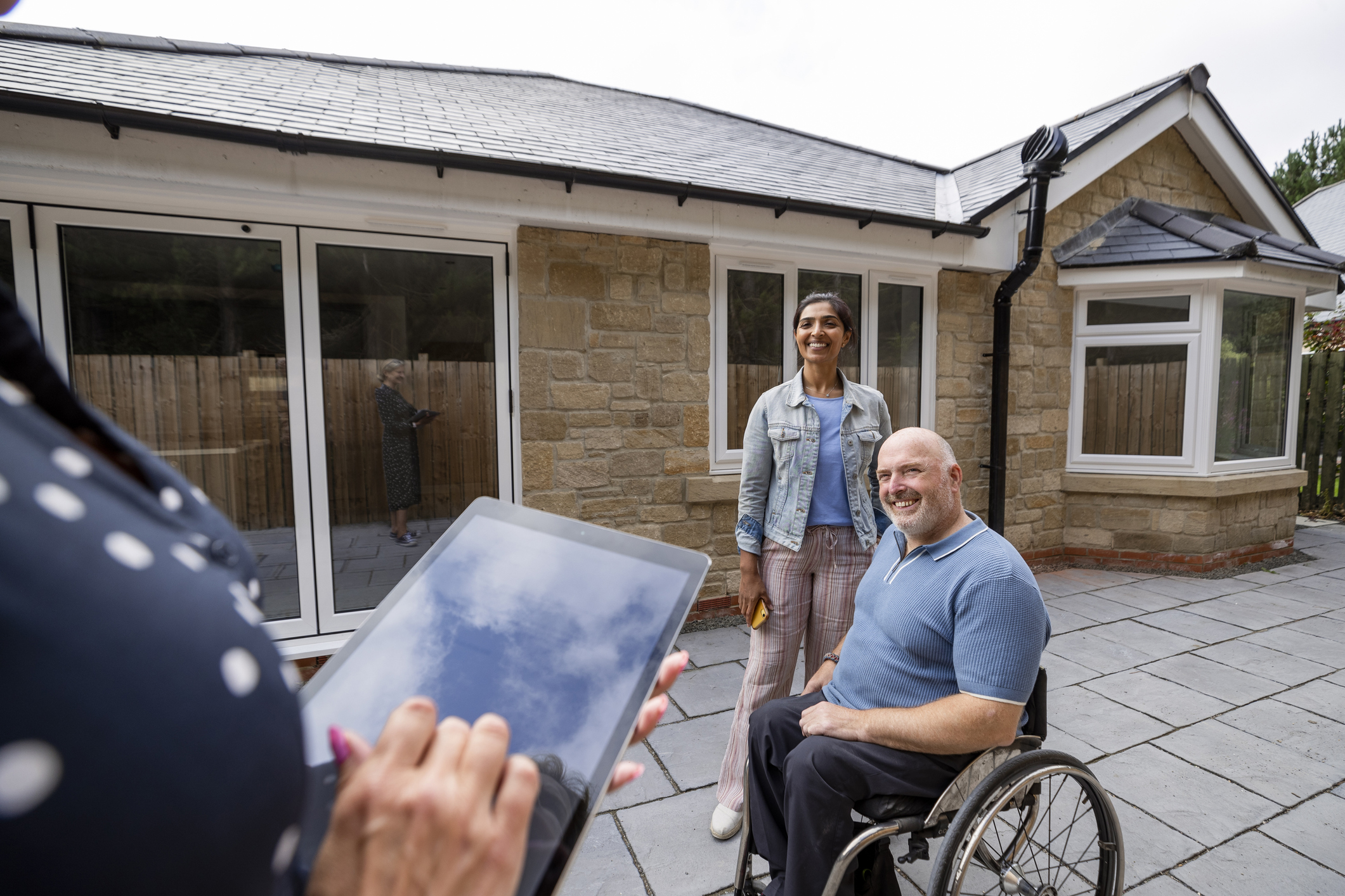 Two people, one in a wheelchair, on patio of a new home. 