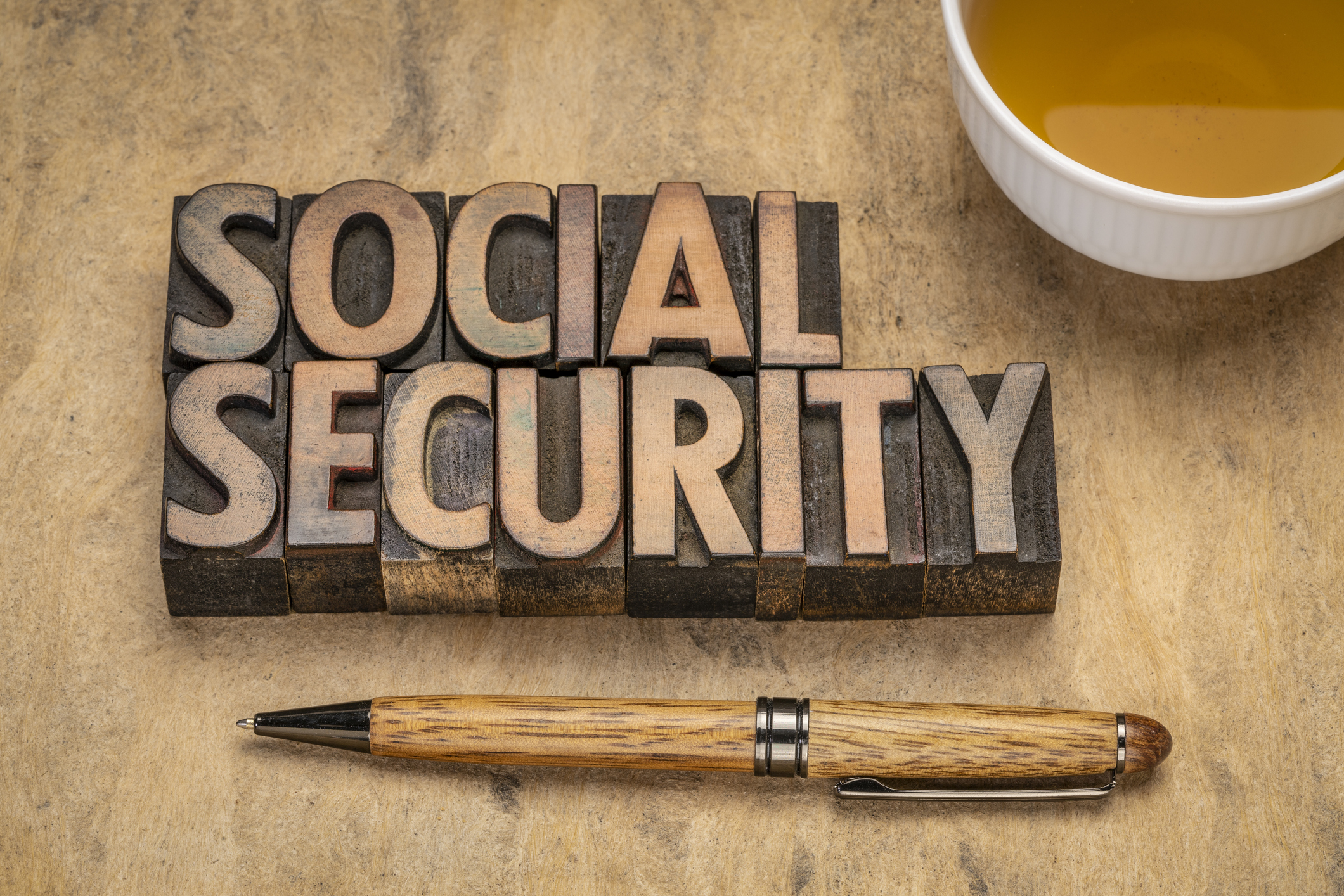 Social Security carved in wood next to a cup of coffee and a pen.