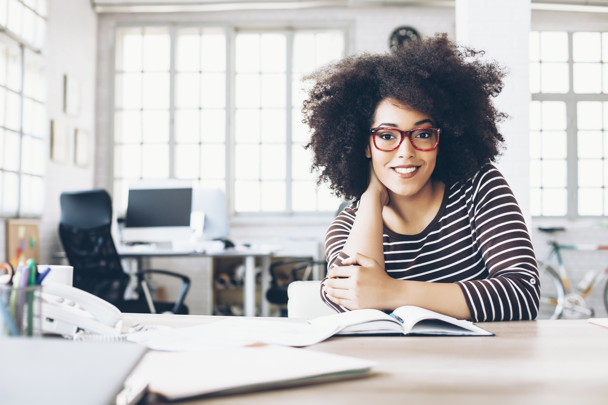 A smiling person at a table with an open book in front of them.