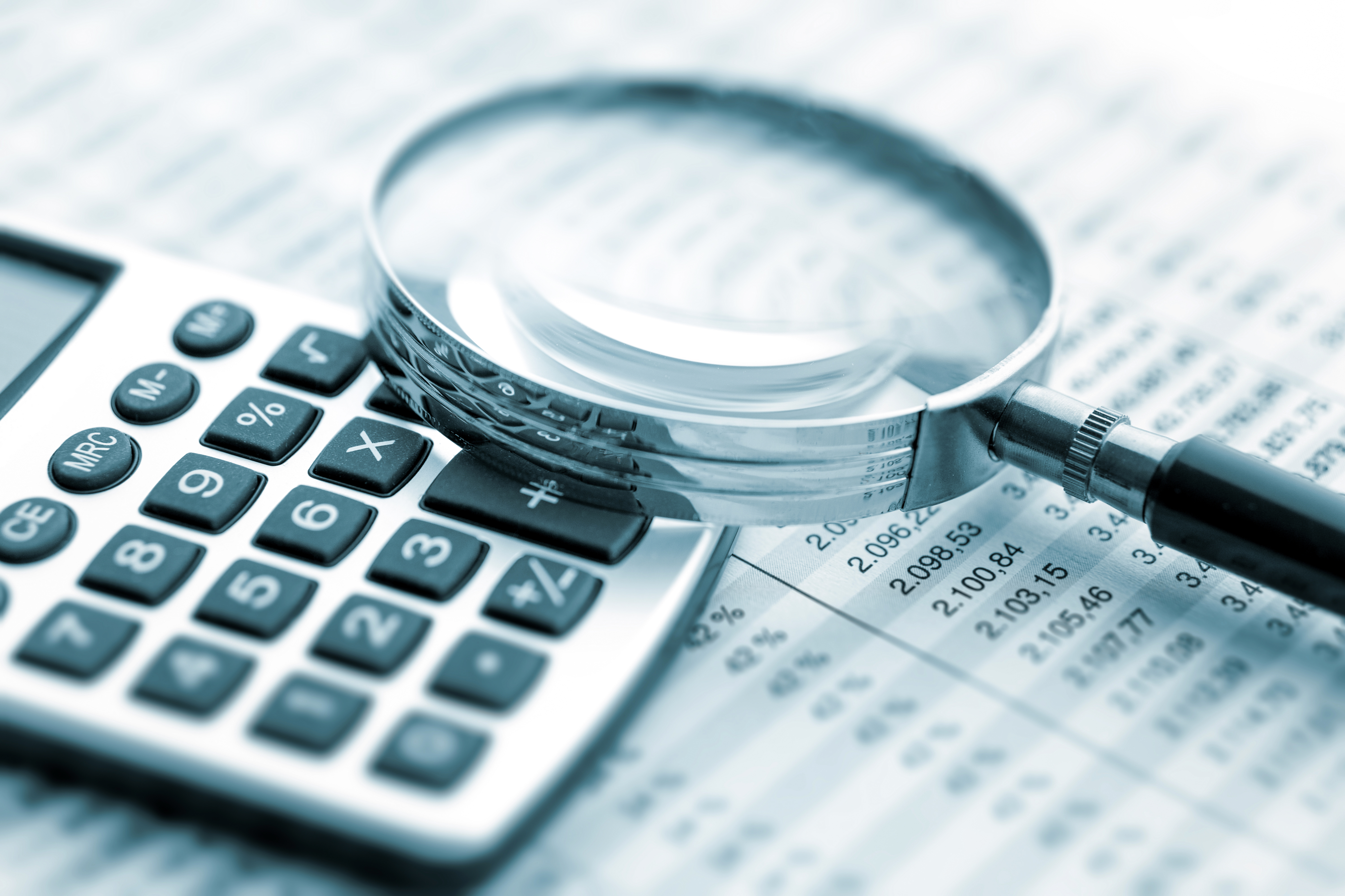 A magnifying glass rests on a calculator, which rests on a document showing itemized sums of money.