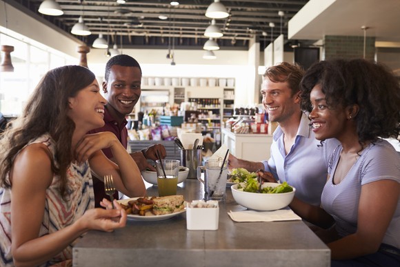 Four friends sitting in a restaurant as a group eating food.