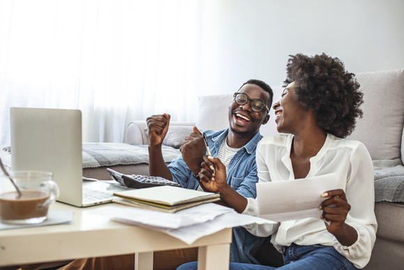 Two people laughing in front of a laptop and paperwork.