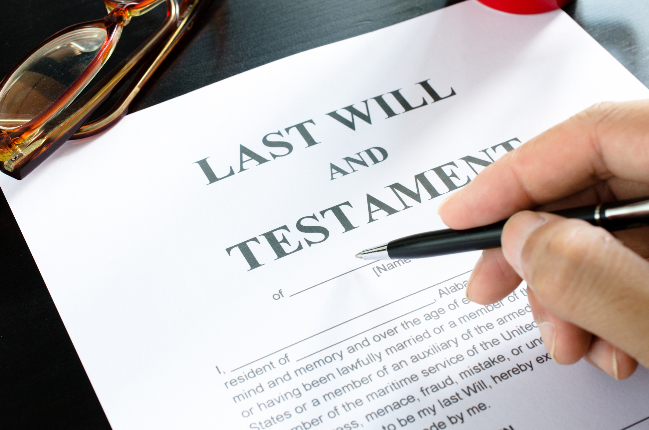 A hand, a pen, and a last will and testament.